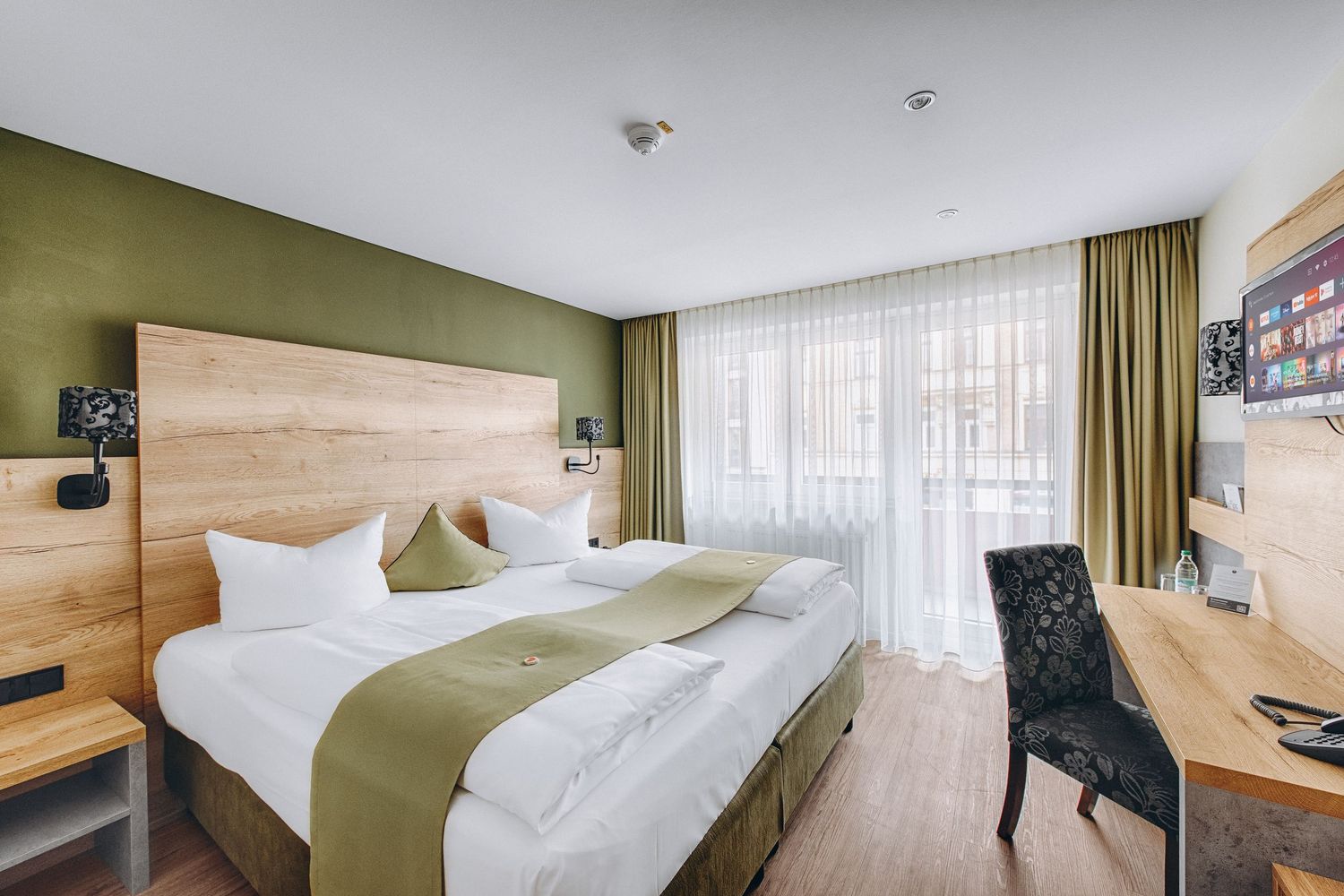 Modern hotel room with white bedding, olive green accents, and wooden headboard panels showcased in multiple room views.
