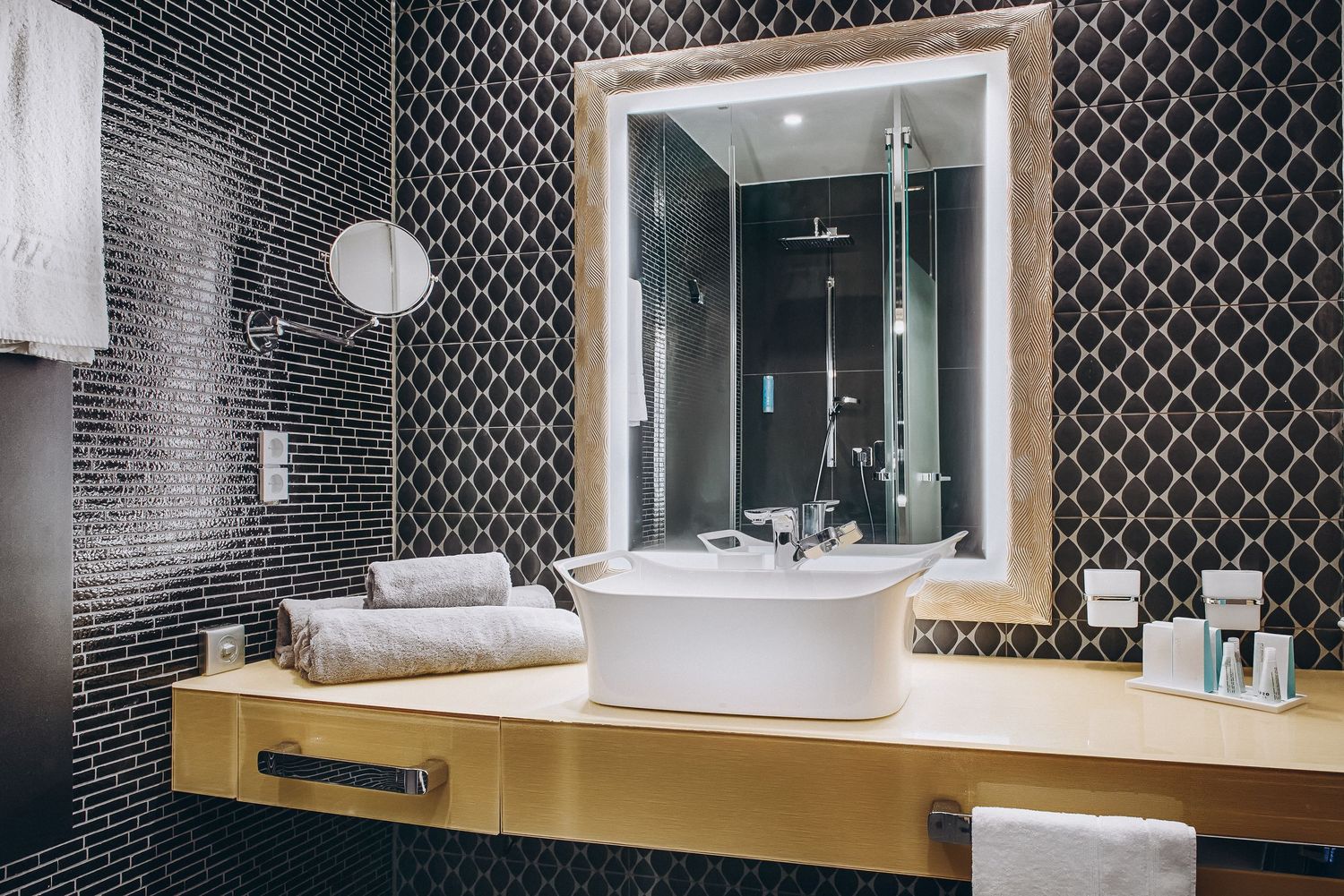 Luxurious bathroom vanity with black patterned wallpaper, wooden countertop and large framed mirror.