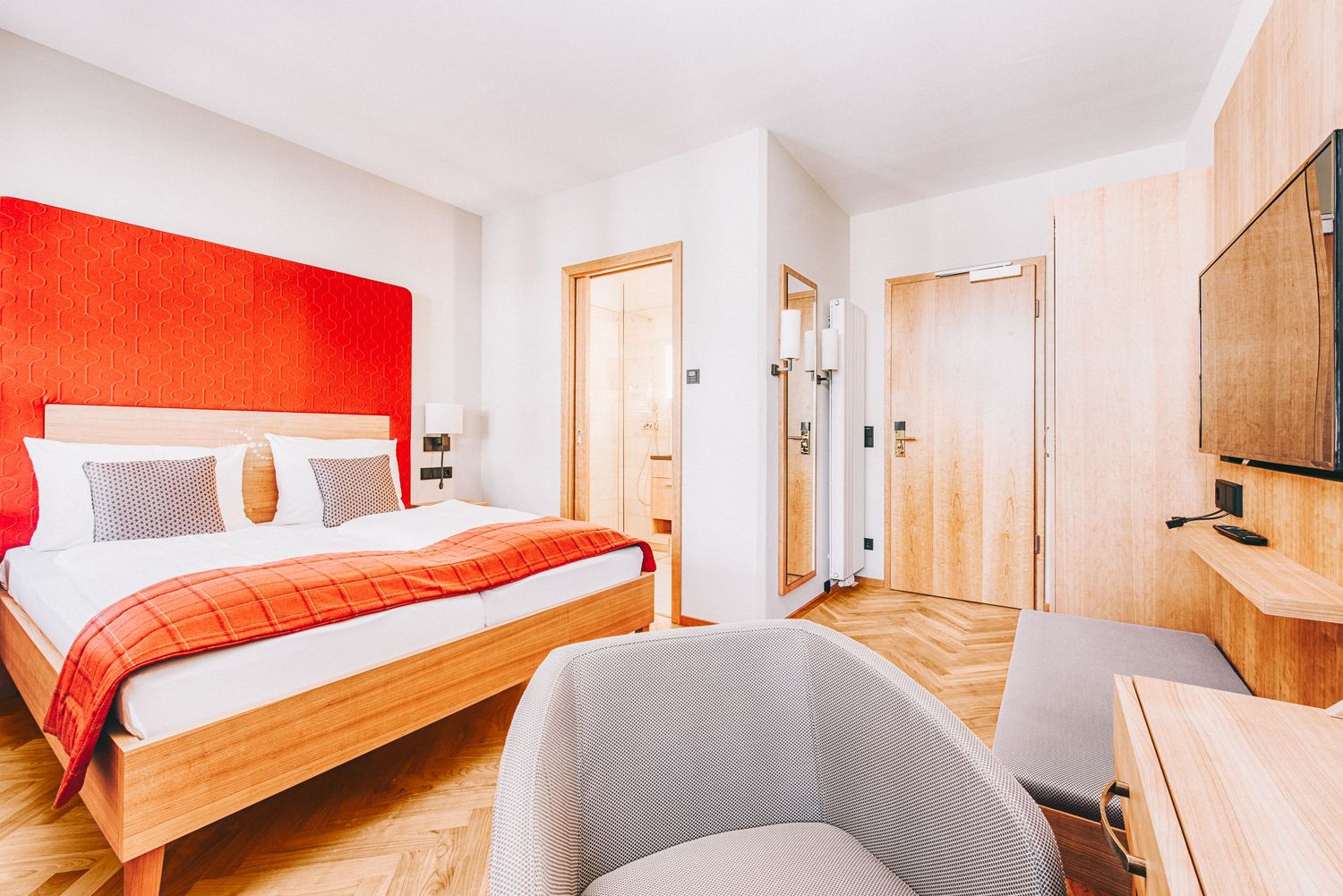 Hotel bedroom with warm wood furniture and vibrant red accents showing multiple viewing angles.