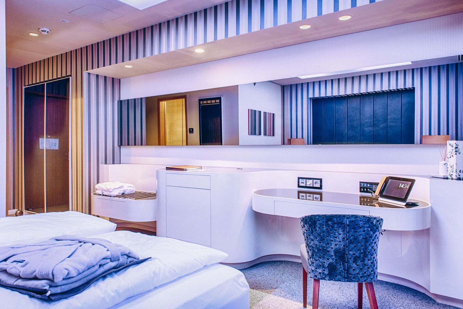 Modern hospital room interior with medical bed, curved desk, and blue chair against striped wall design.