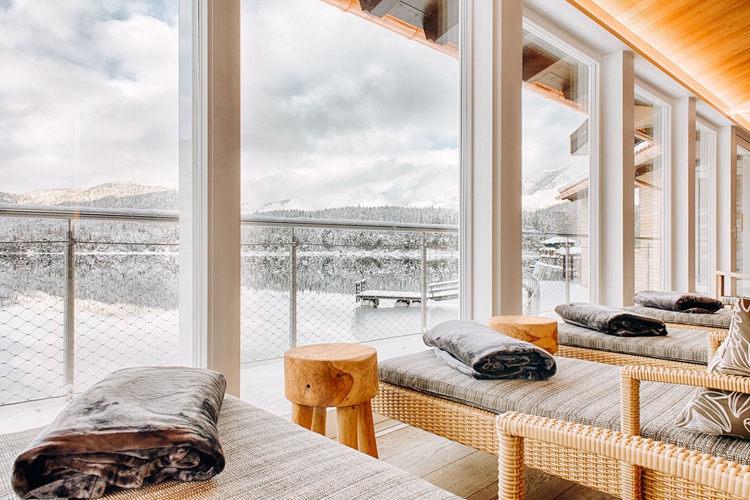 Luxury spa lounge chairs overlooking a snowy winter landscape with panoramic windows and wooden ceiling beams.