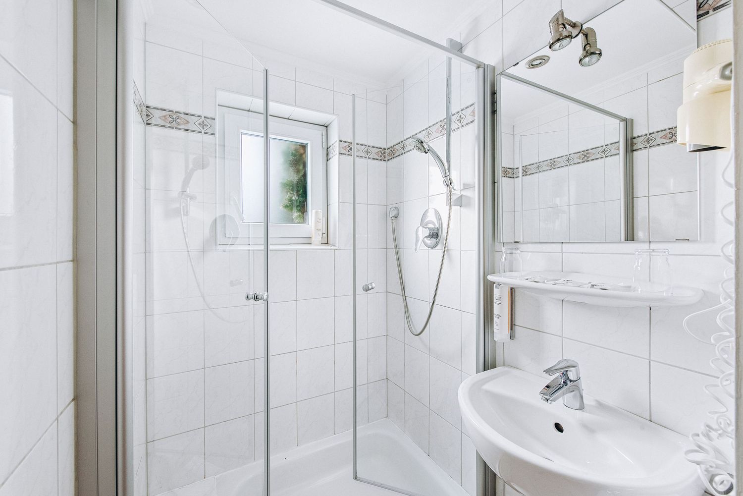 Modern white bathroom interior with glass shower enclosure, wall-mounted sink, and ceramic tile walls and floor.