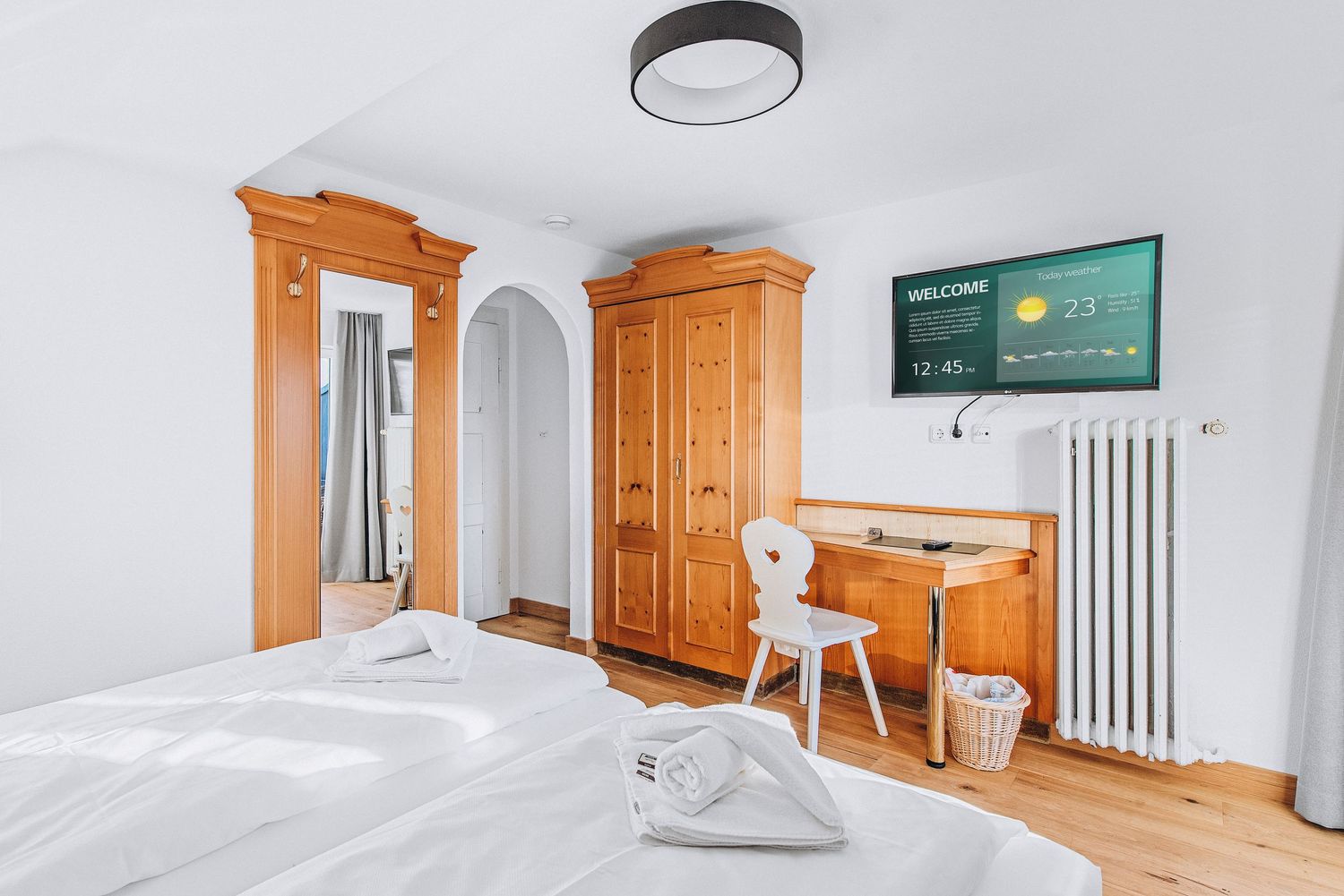 Modern hotel room interior with wooden furniture, white walls, and mounted TV features traditional Alpine design elements.
