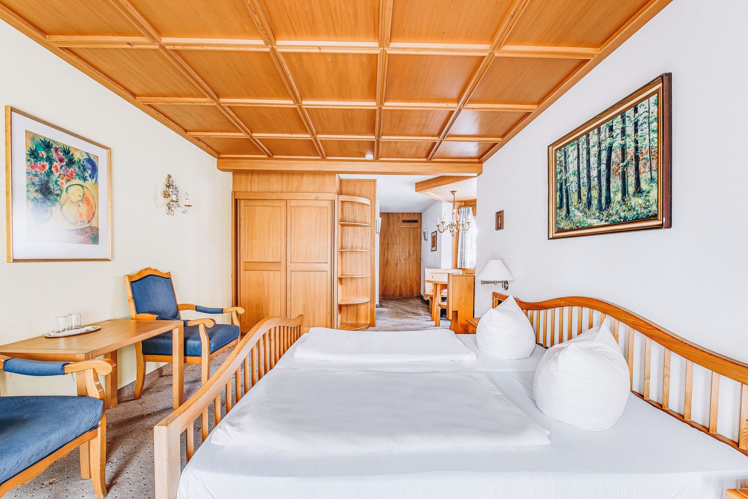 Hotel room interior featuring wooden ceiling beams, white walls with framed artwork, and twin beds with wooden railings.