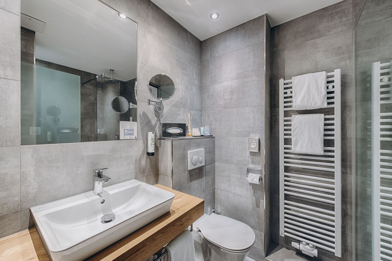 Modern grey bathroom with wooden vanity, white sink, heated towel rail and concrete-style tiled walls.