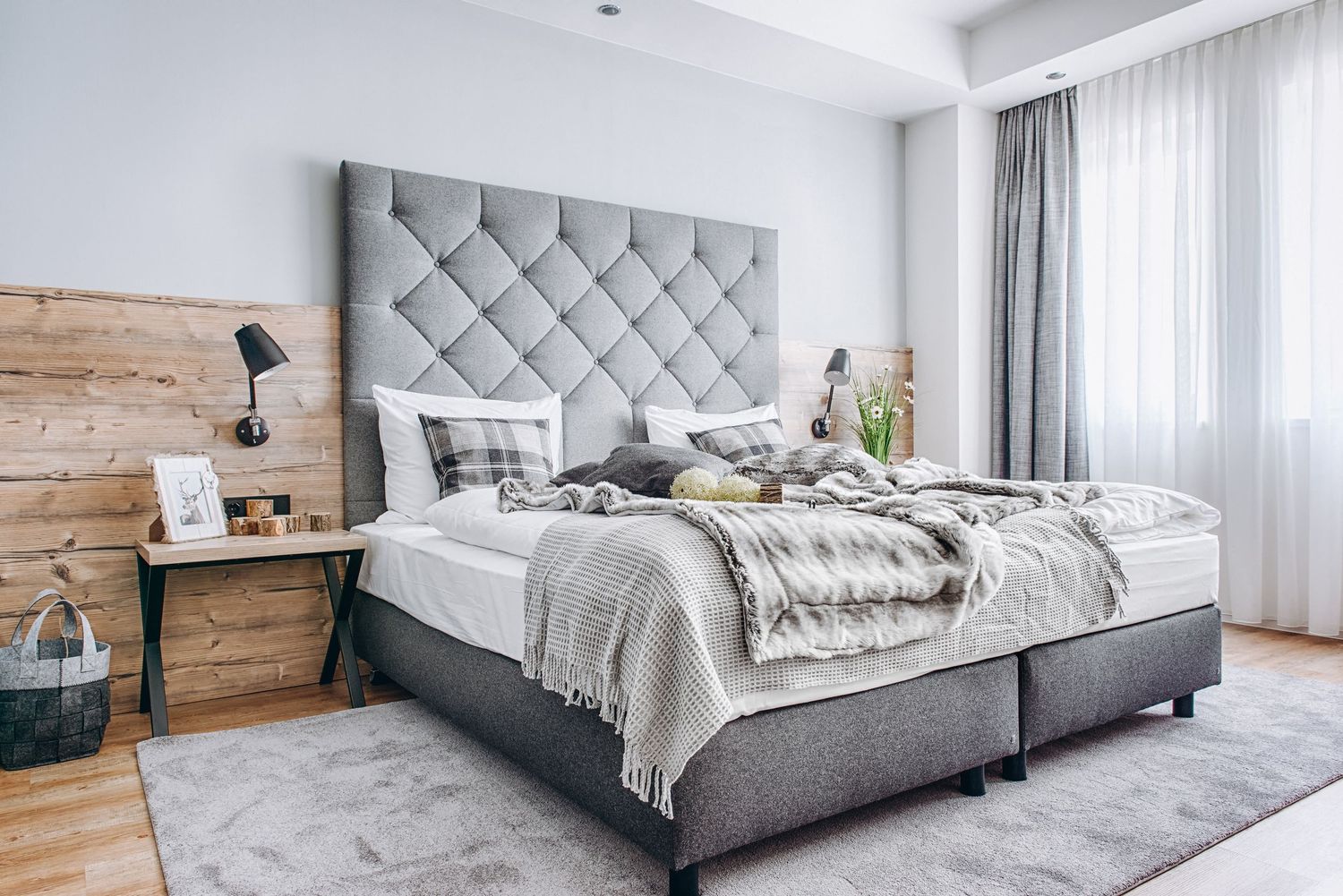 Modern bedroom interior featuring a gray upholstered bed with wooden accent wall and white bedding.