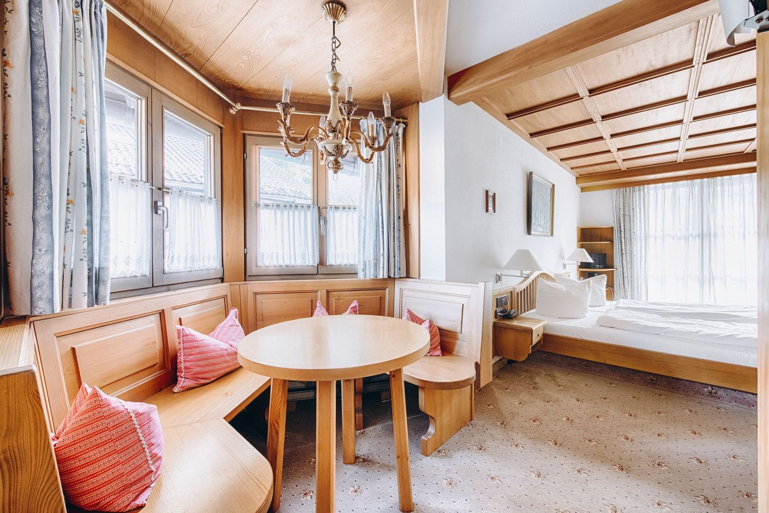 Cozy alpine dining nook with built-in wooden bench seating, round table, red cushions and chandelier in rustic room.