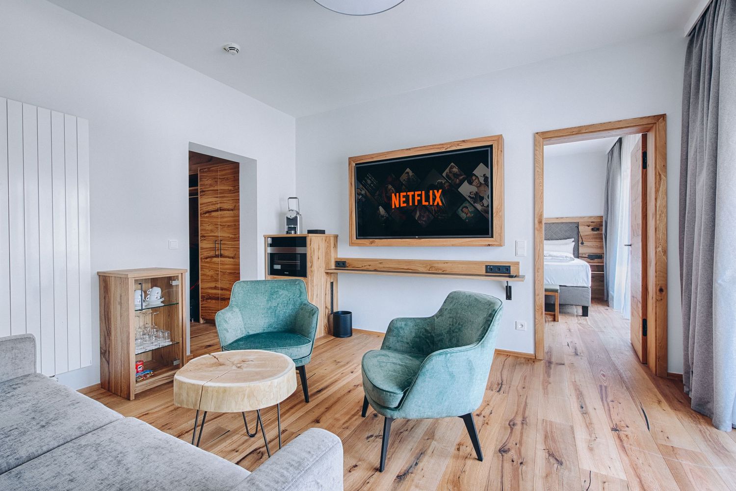 Contemporary hotel room lounge area with Netflix TV, turquoise armchairs and hardwood flooring.