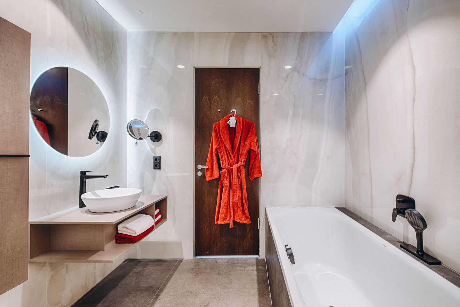 Modern bathroom interior with freestanding tub and red bathrobe on display.