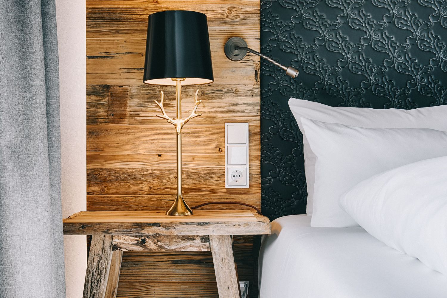 Modern bedside table with black lamp against wooden wall and dark textured headboard in contemporary bedroom setting.