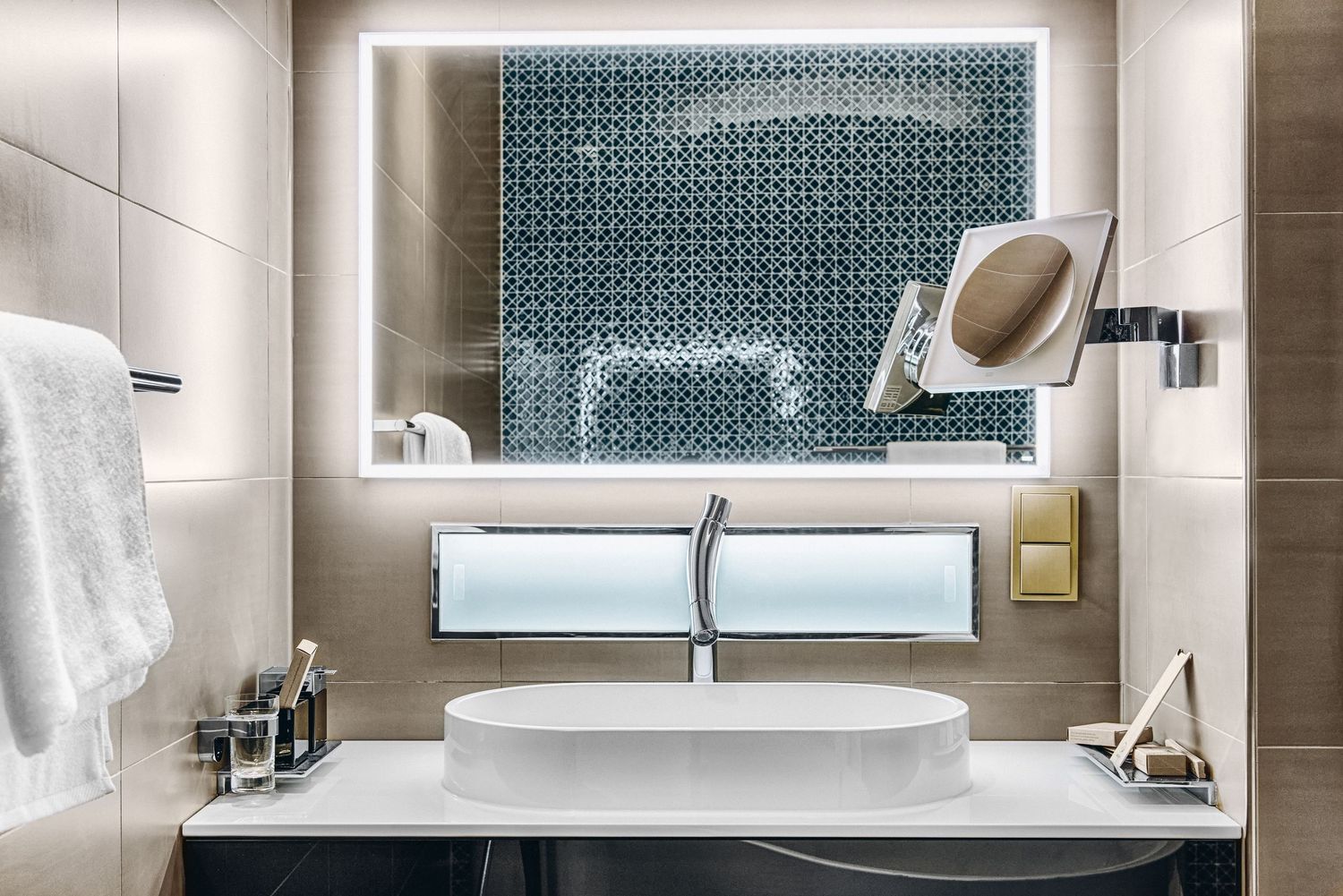 Sleek bathroom vanity with illuminated mirror, textured wall tiles, and modern chrome fixtures in neutral tones.