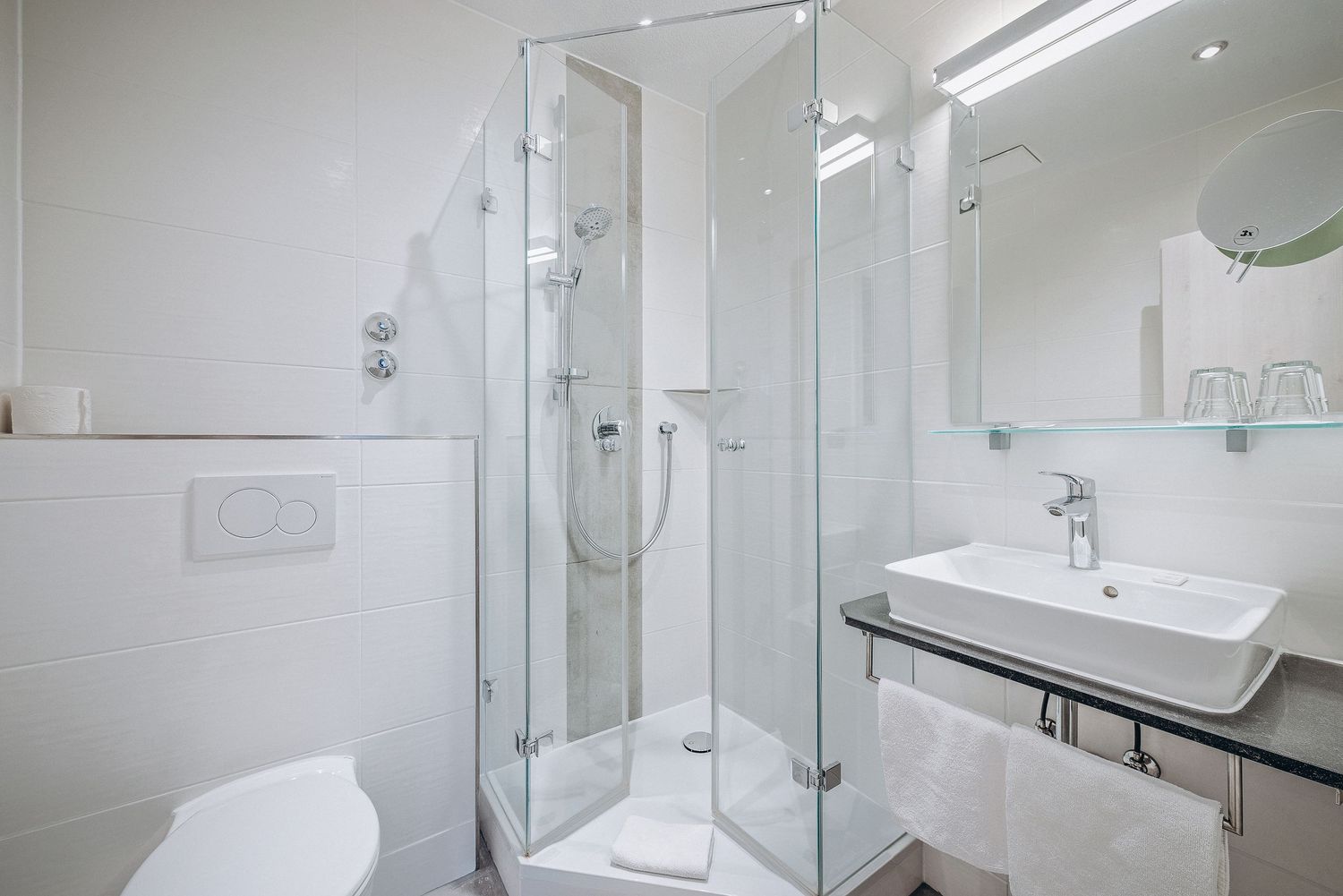 Modern minimalist bathroom interior with glass shower enclosure, white vessel sink, and clean white tiled walls.
