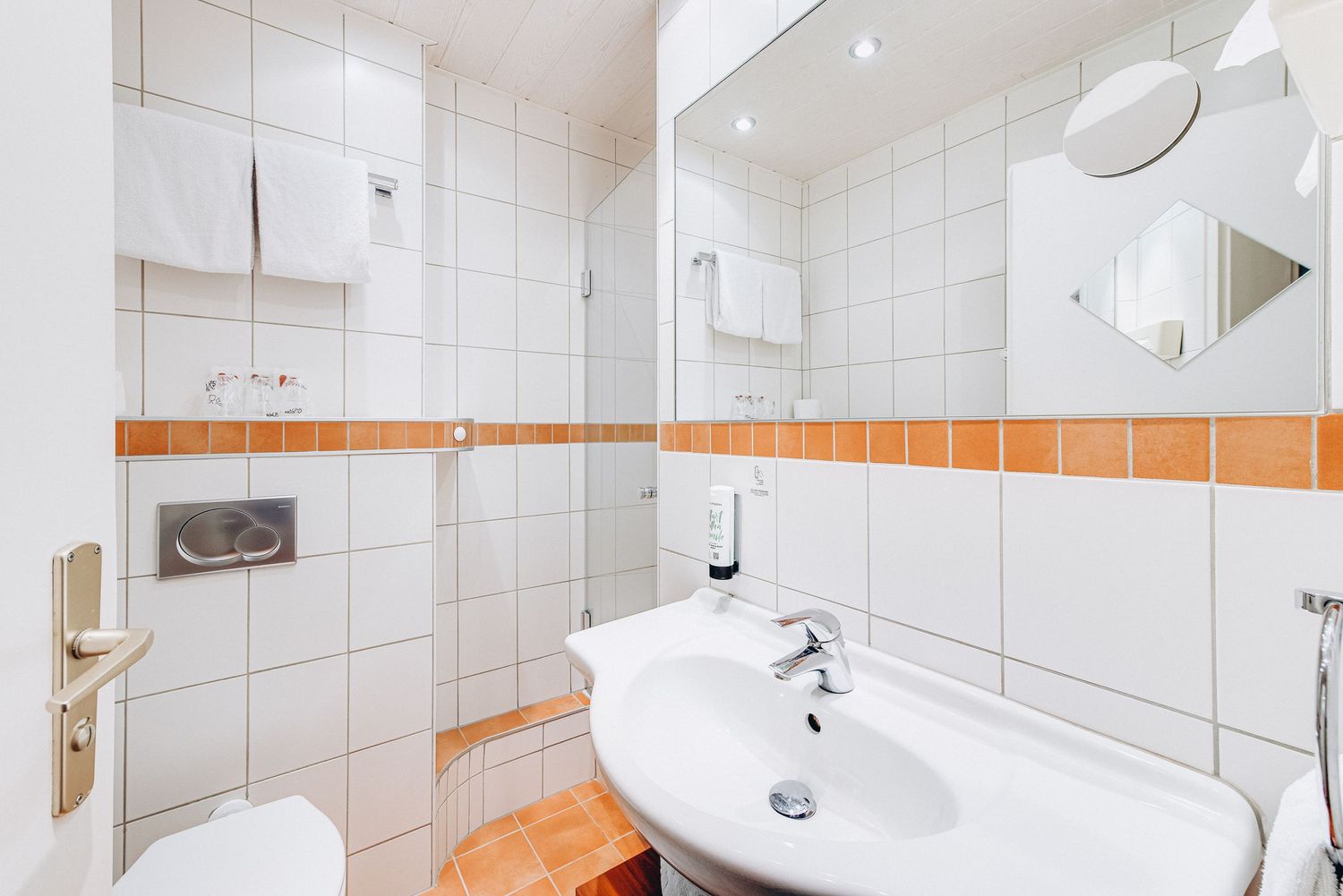 Clean white and orange bathroom with tiled walls, modern fixtures, and a round mirror.