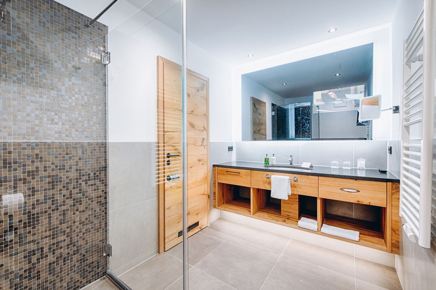 Contemporary bathroom interior with mosaic tile walls and wooden built-in storage elements.