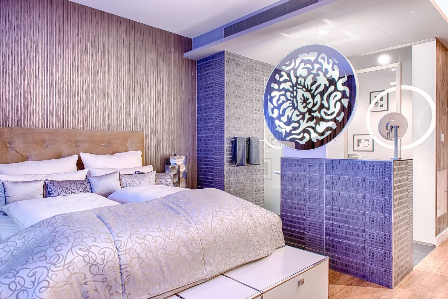 Modern hotel bedroom with blue accent wall and large circular art piece featuring elegant white and silver decor.