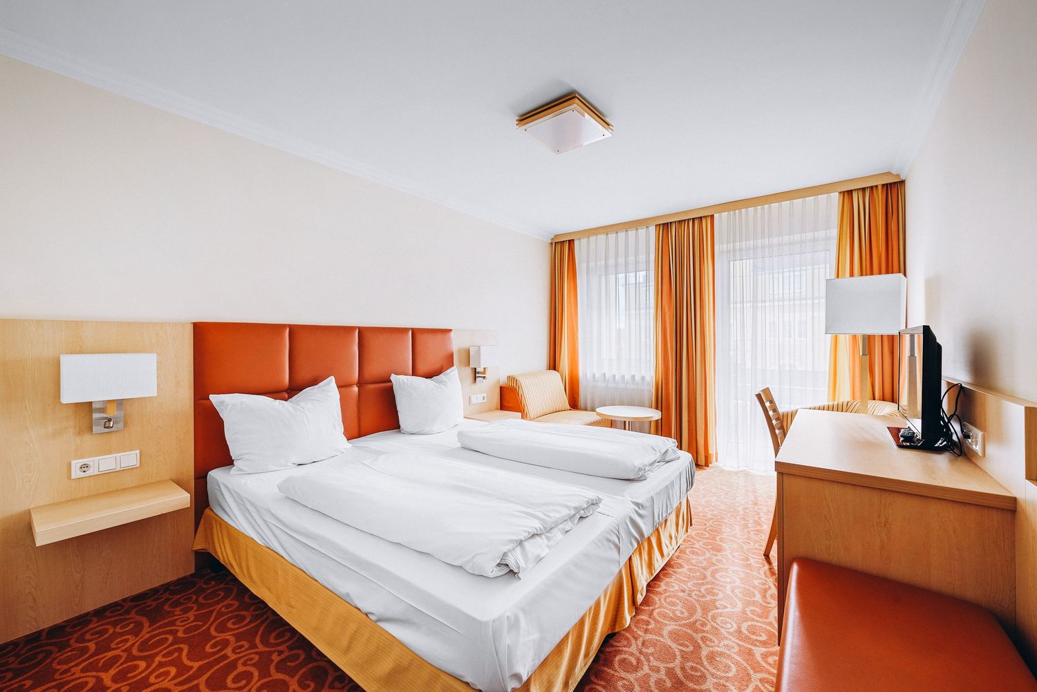 Bright hotel room with orange accents, white bedding, and wooden furnishings.