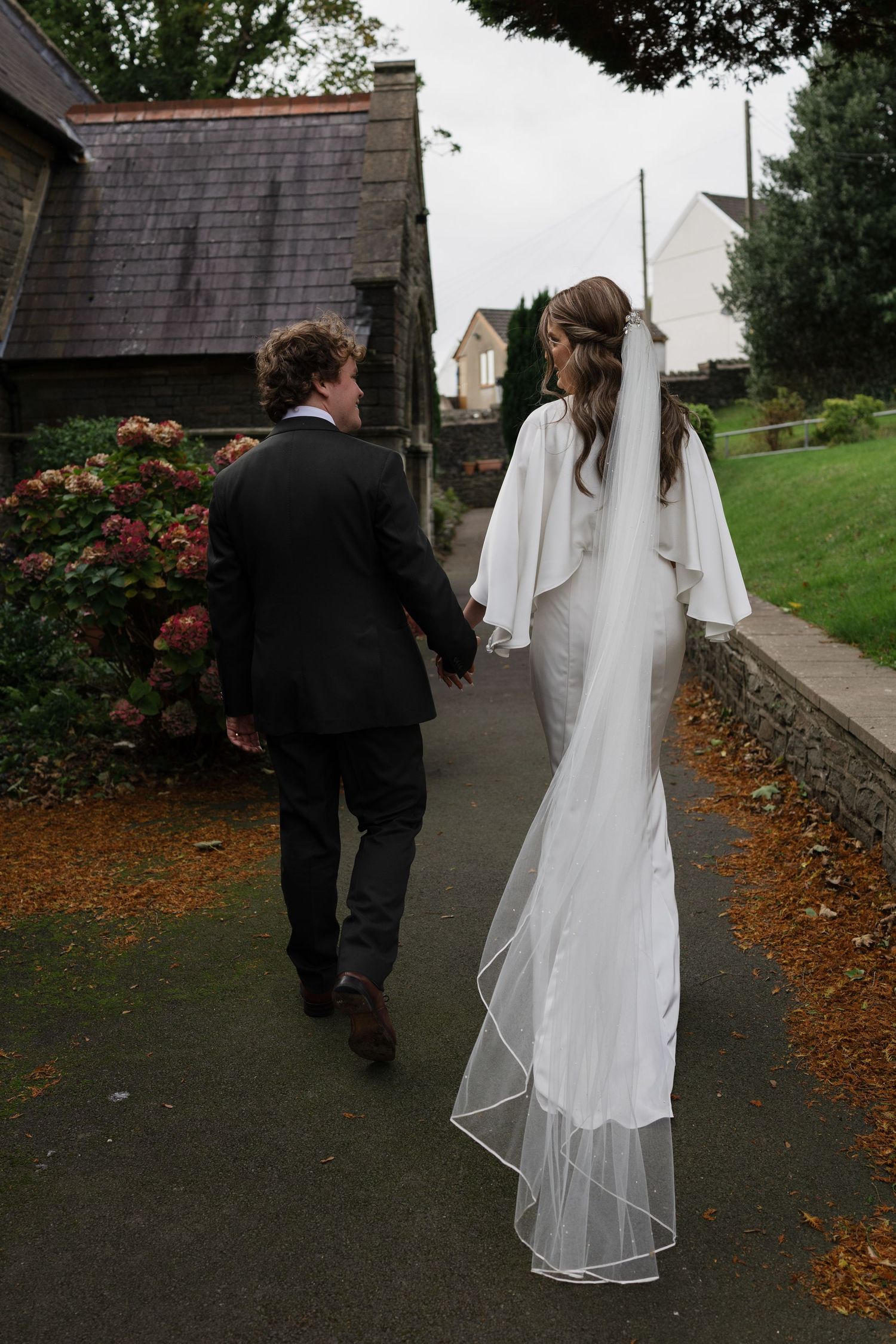 A couple walks along a garden path after their wedding ceremony.