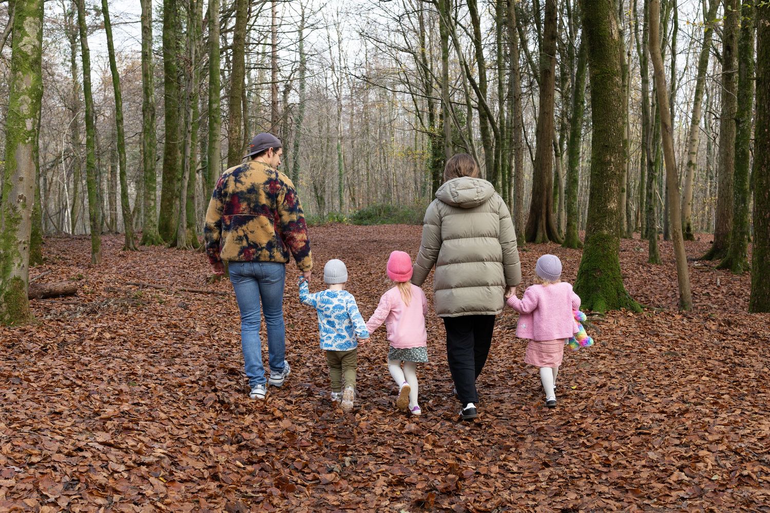 A family walks through a forest path covered in autumn leaves.