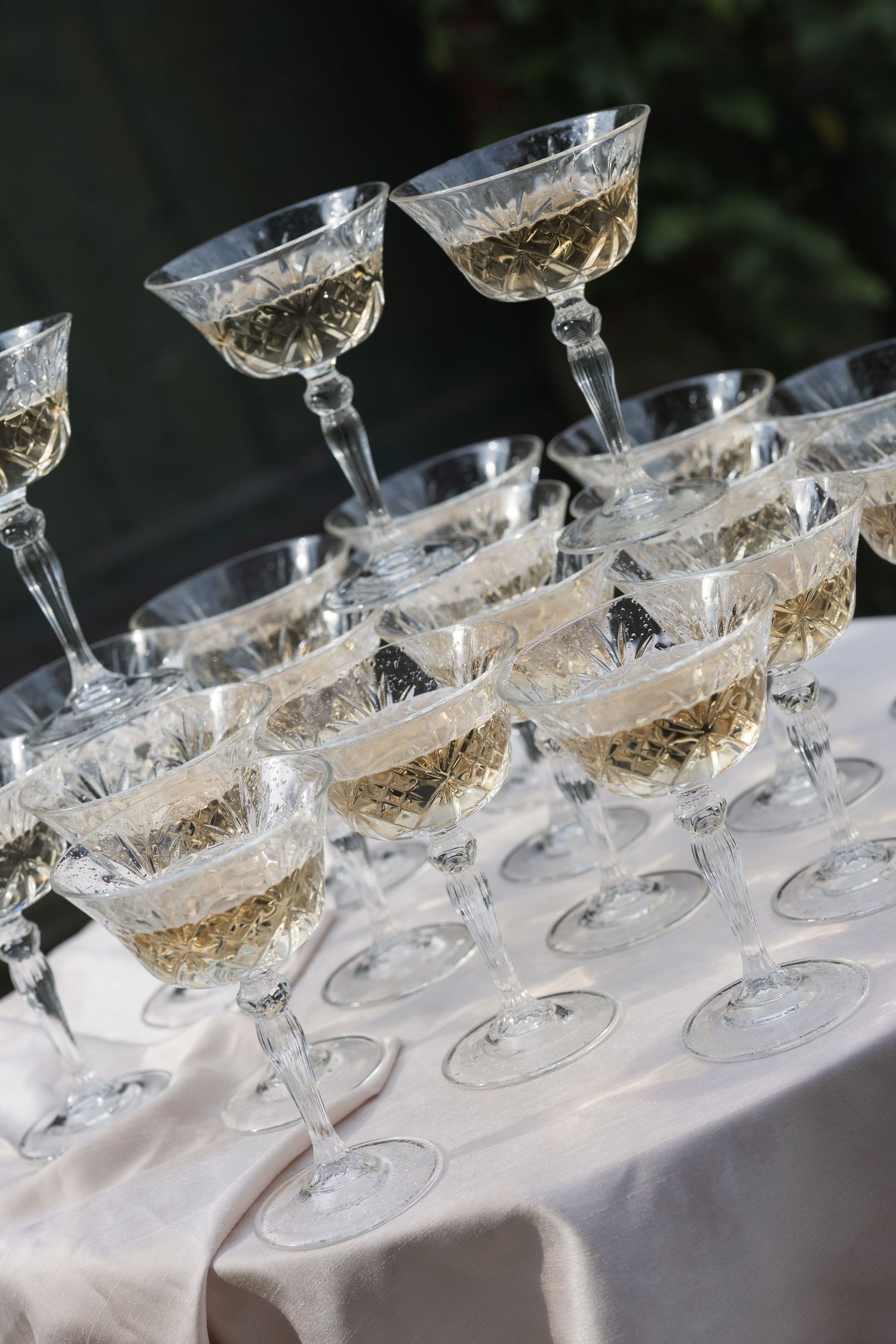 Elegant crystal champagne glasses filled with white wine arranged on a white tablecloth at an event.