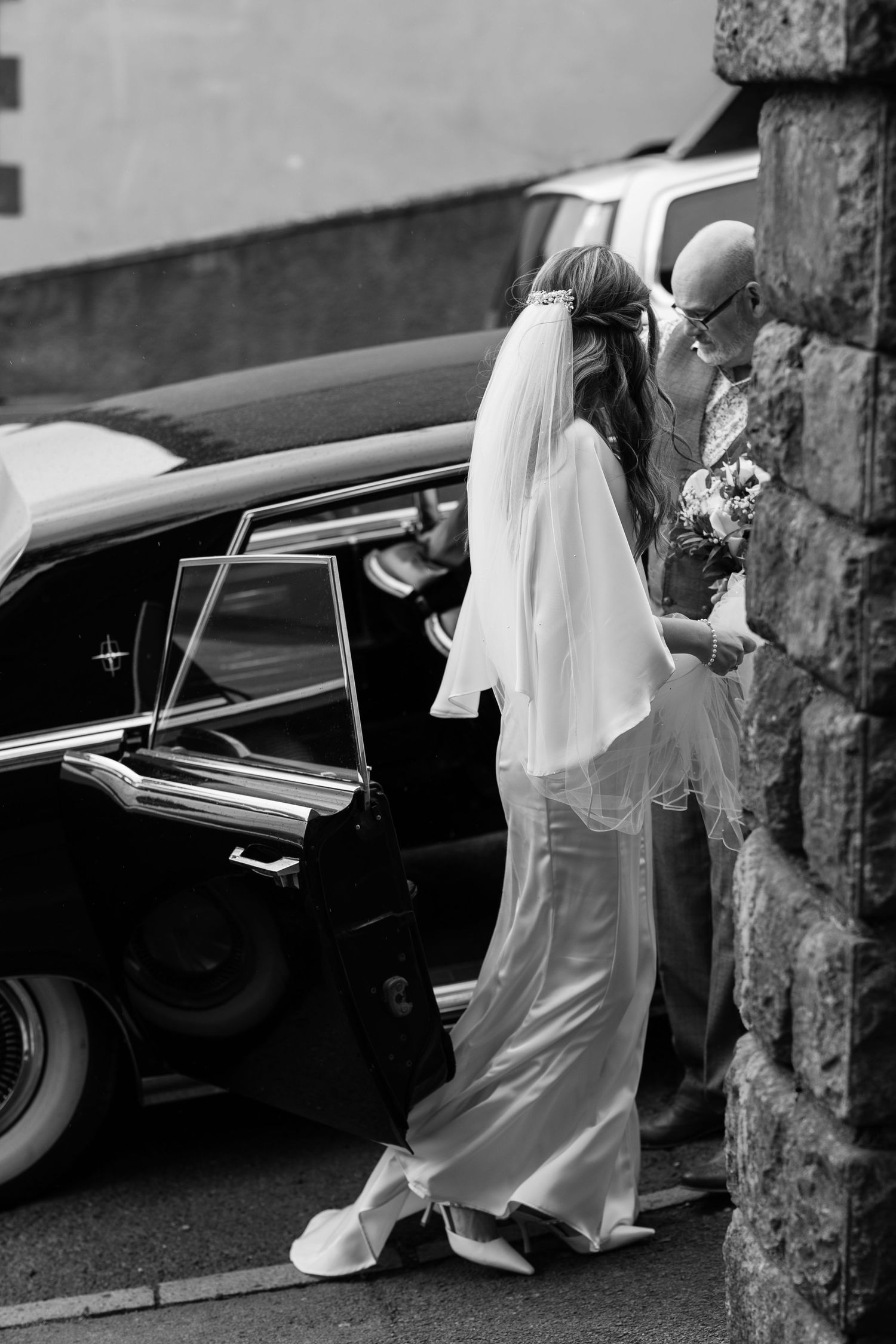 A bride in an elegant white dress arrives at her wedding venue.