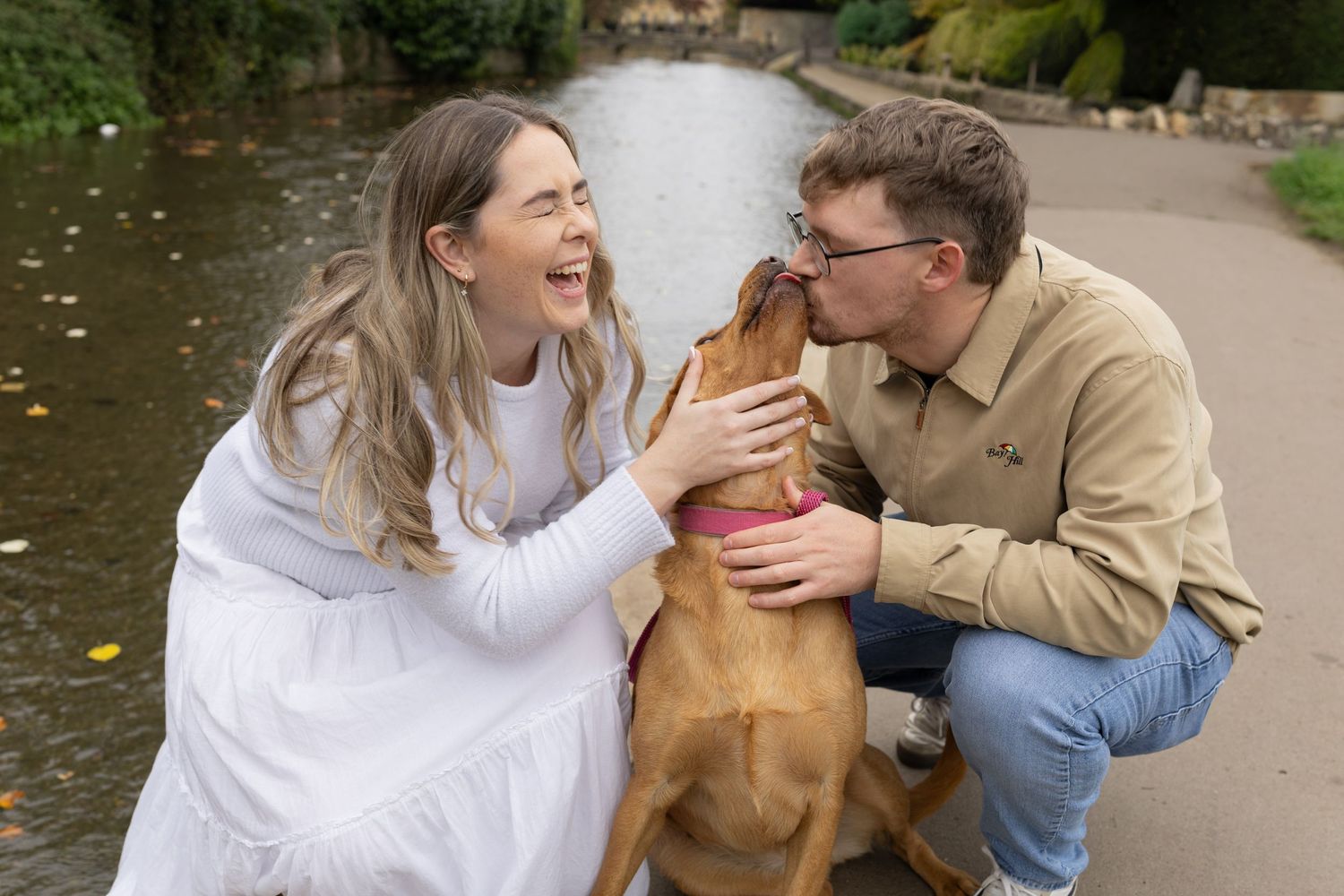 A couple shares a joyful moment with their golden retriever dog in a park setting.