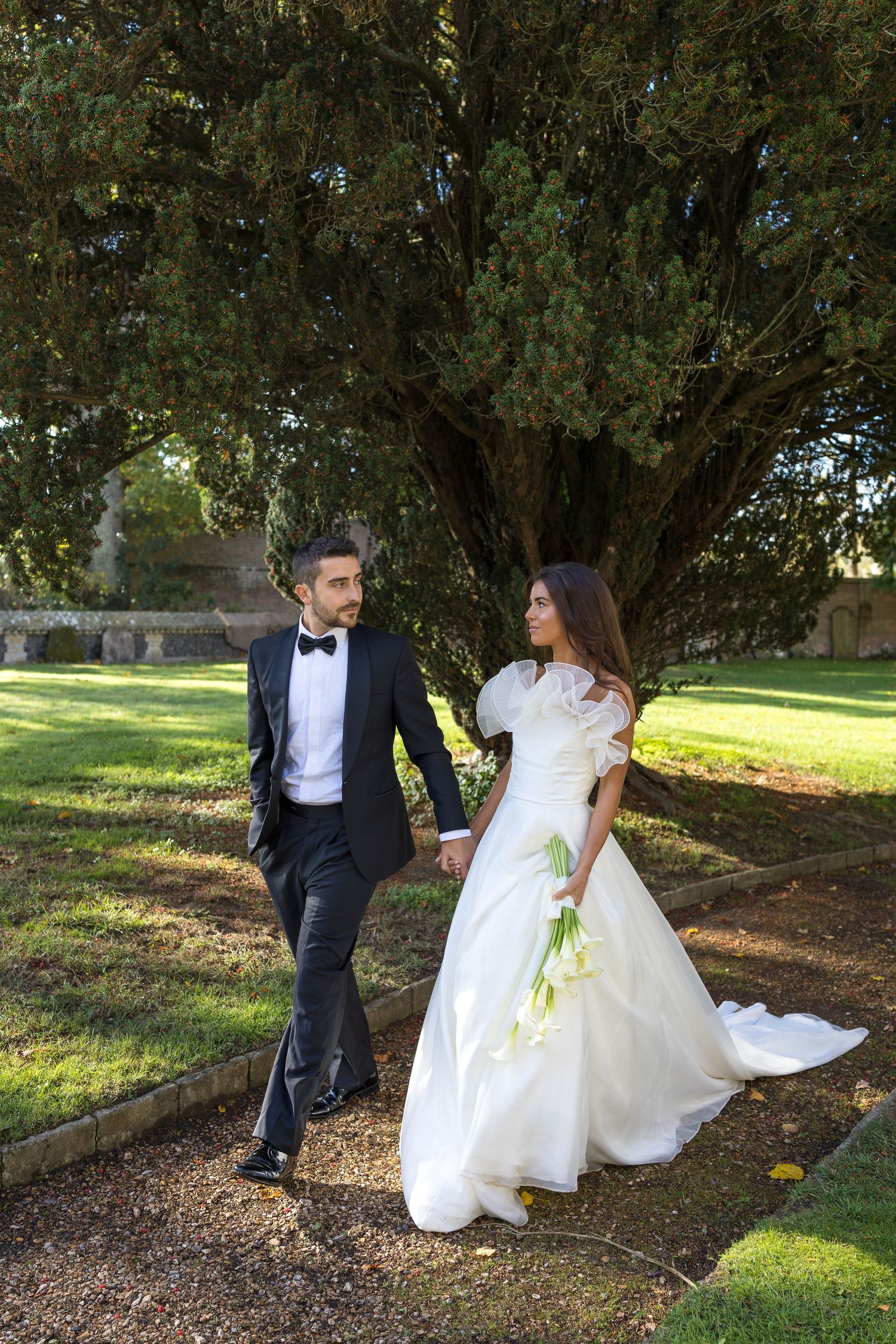 Wedding couple walking through a garden with sunlight filtering through trees.