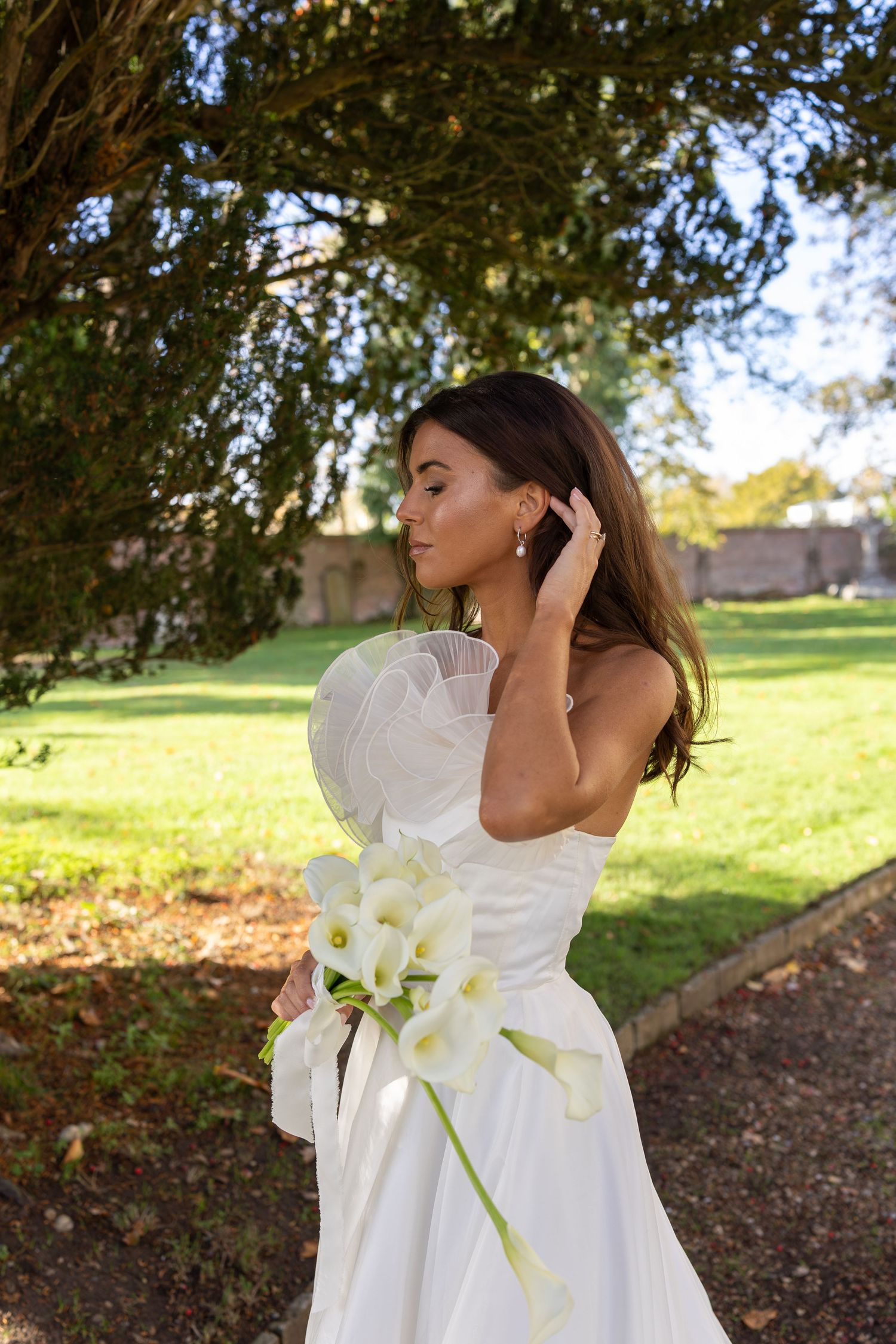 Bride in flowing white dress with calla lilies in outdoor garden setting.