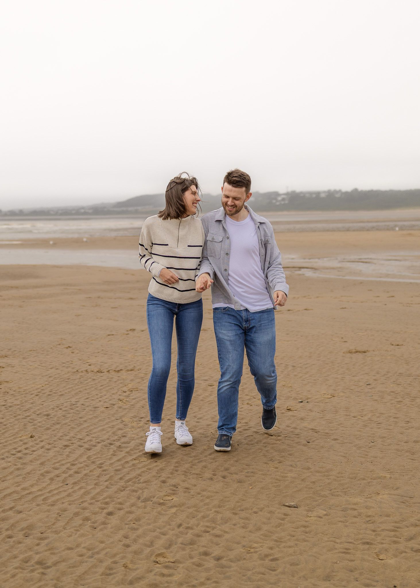 Couple walking together on a vast empty beach on an overcast day.