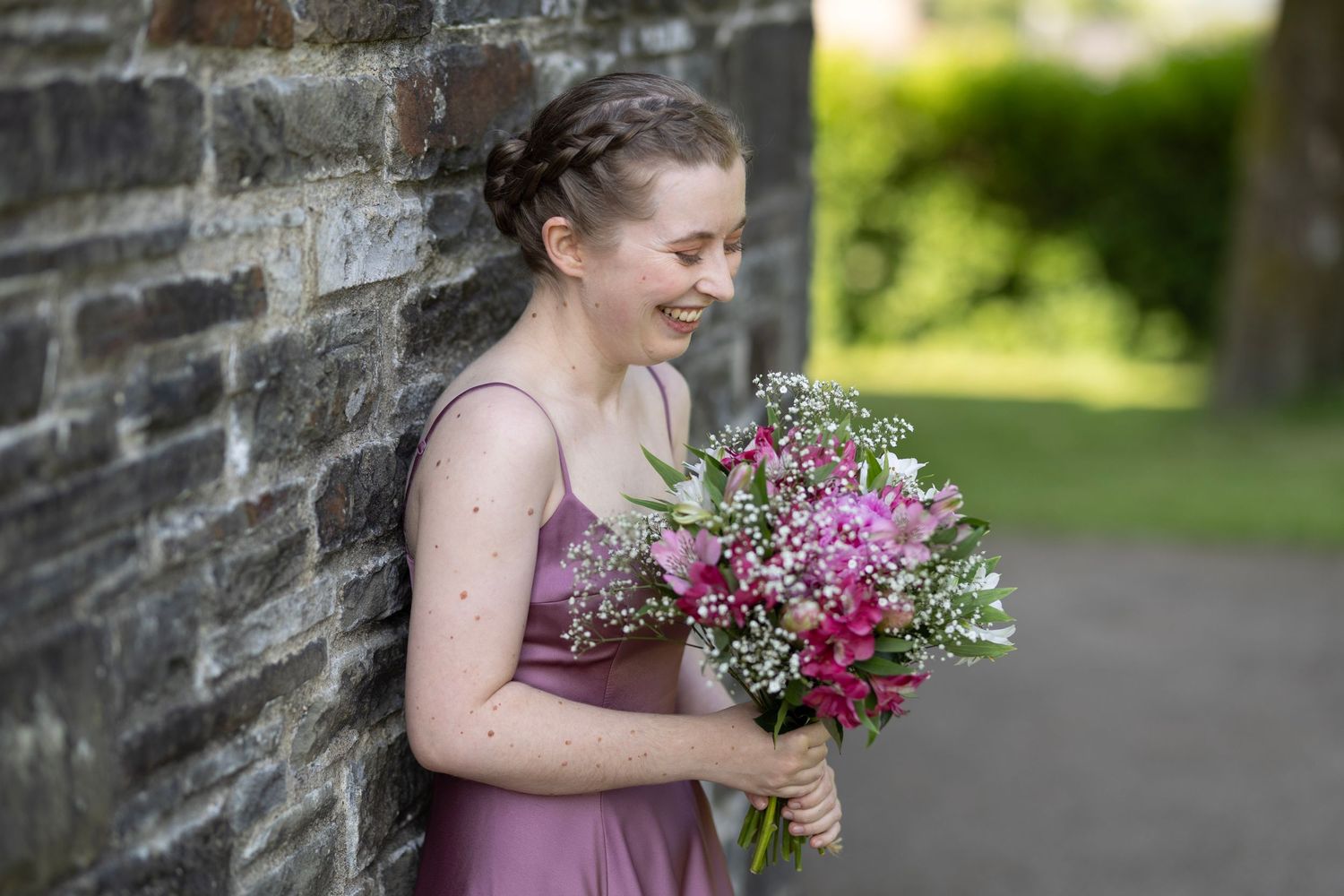 Person in a mauve dress holding a vibrant bouquet against a stone wall background.