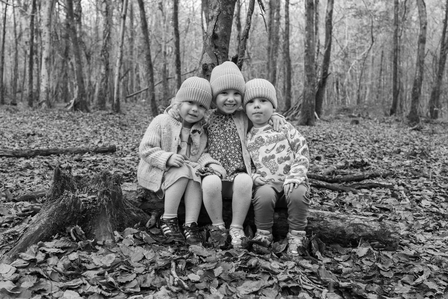 Family members sit together on a fallen log in a winter forest setting.