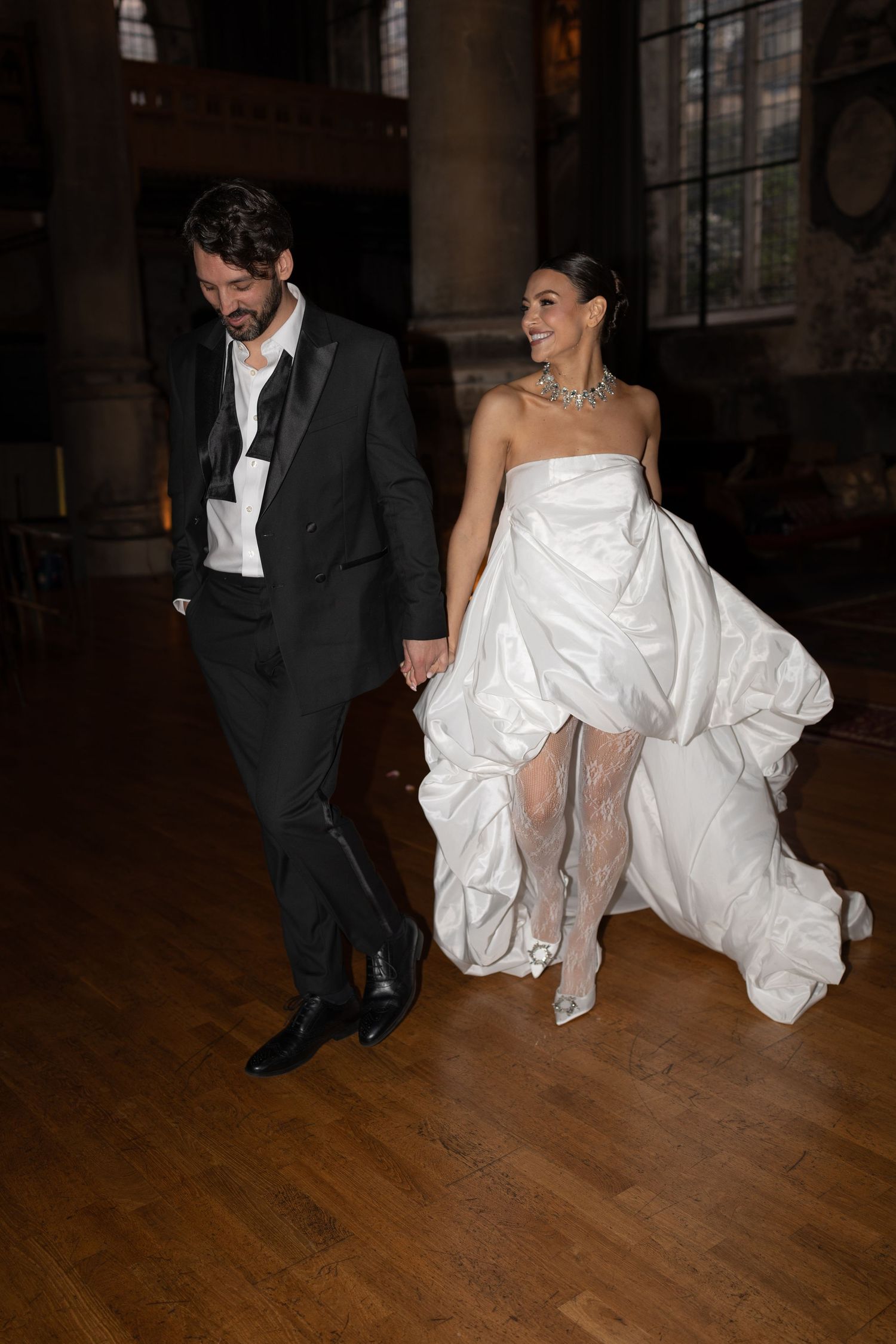A couple dancing at a wedding, with the bride in a flowing white dress and groom in dark suit on a wooden dance floor.
