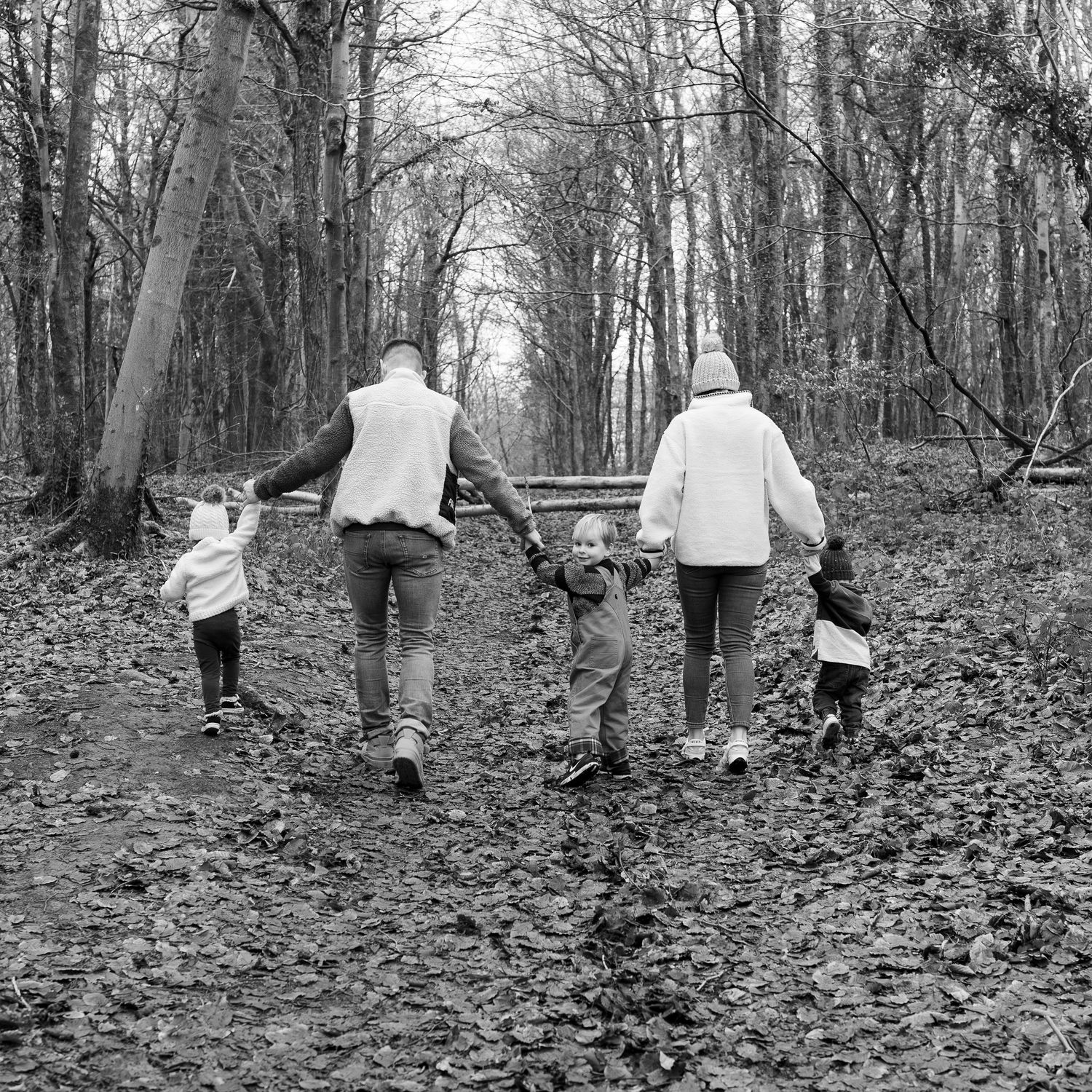 Black and white image of people walking through a leaf-covered forest path.