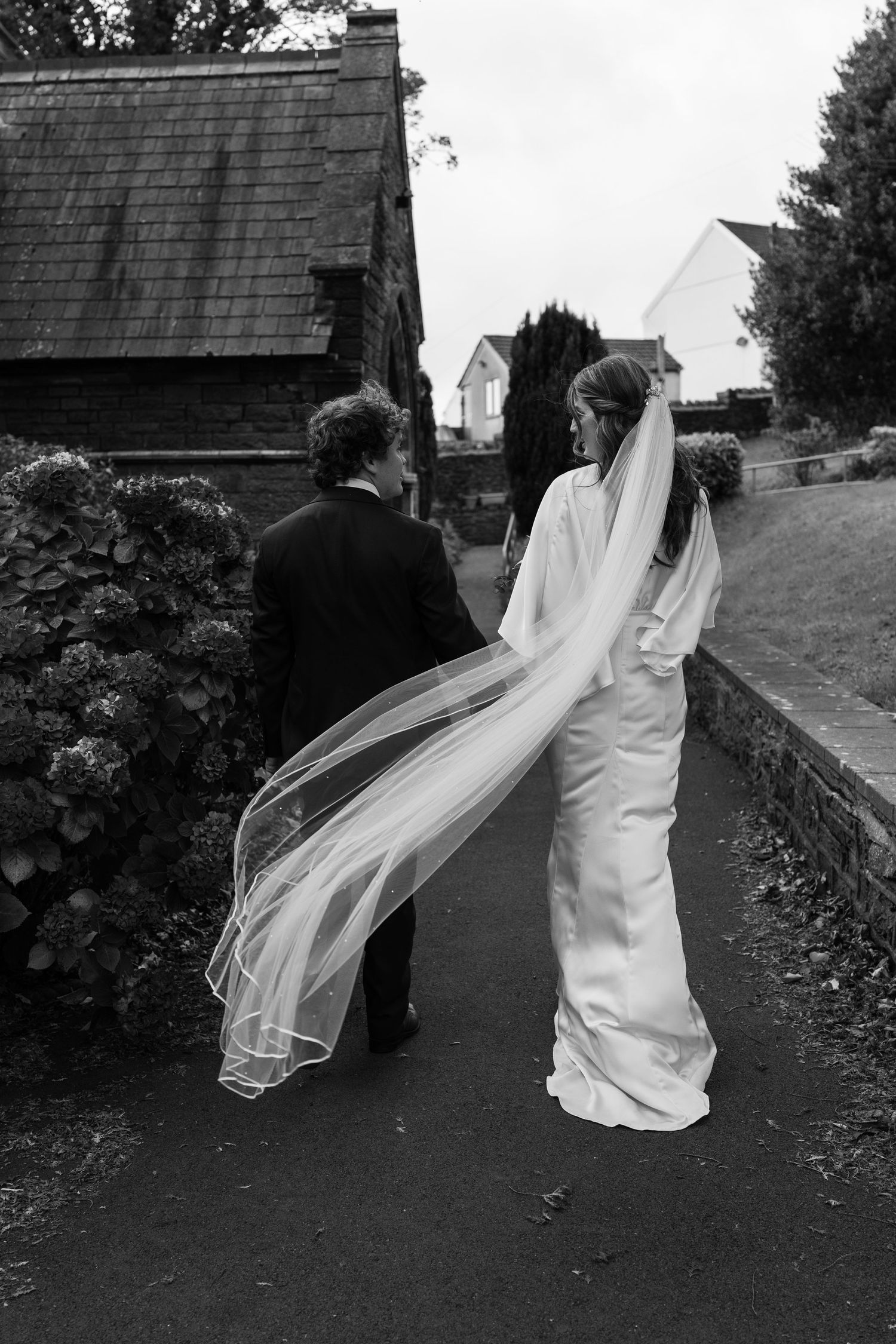 Black and white wedding photo showing flowing veil movement against rustic buildings.