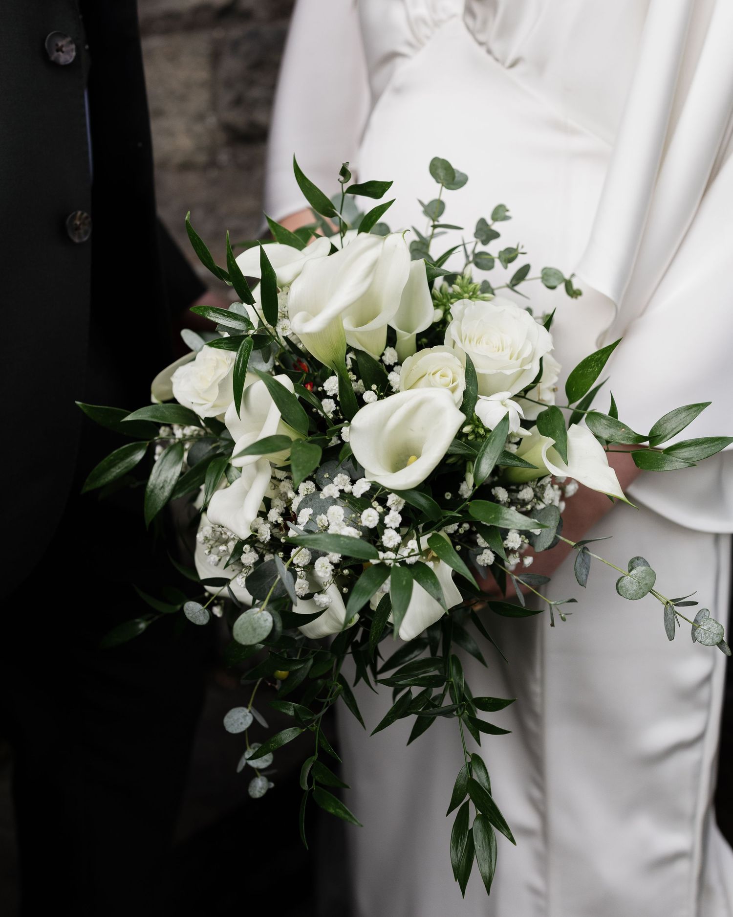 An elegant white wedding bouquet with roses, calla lilies and eucalyptus.
