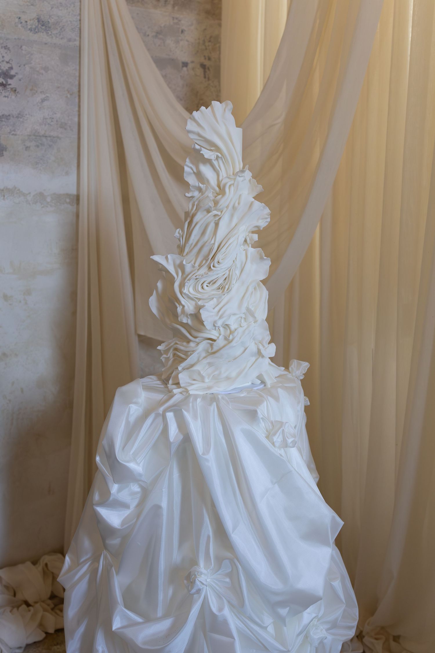 Close-up details of white wedding cake with intricate fabric ruching and folds.
