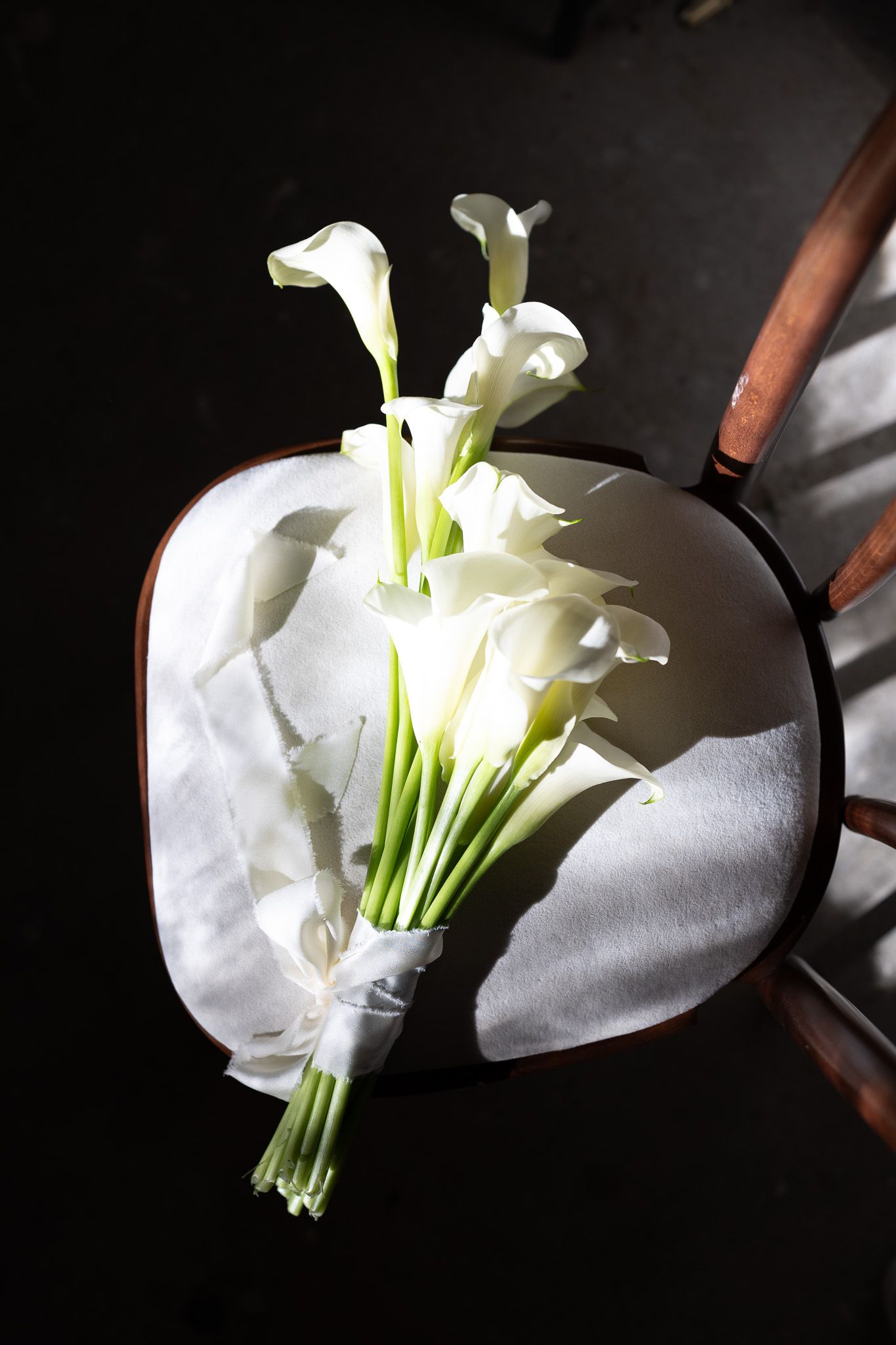 Elegant white calla lilies arranged against a dark background with dramatic lighting.