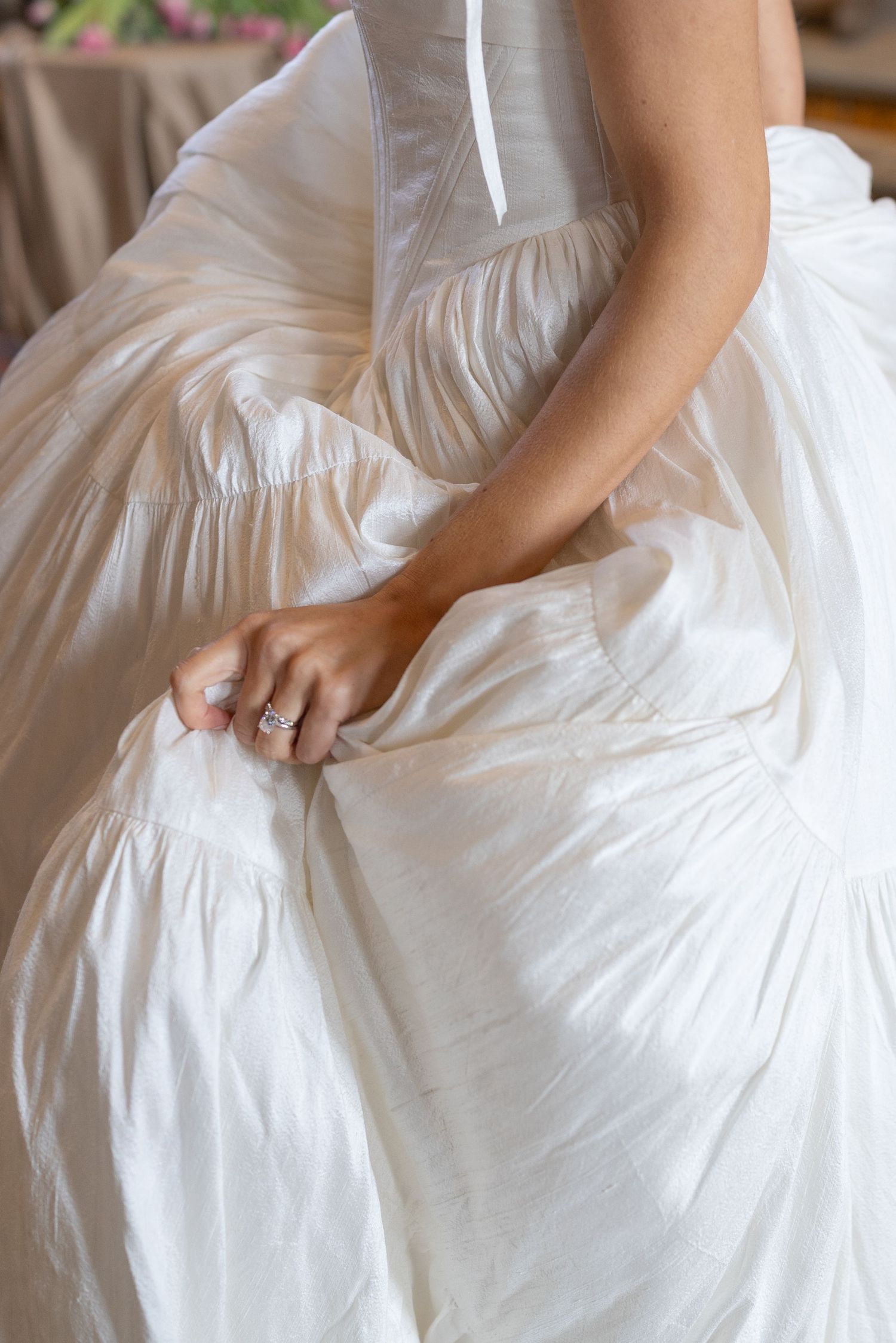 Close-up view of brides hands picking up her flowing wedding dress with her wedding ring and engagement ring in focus.