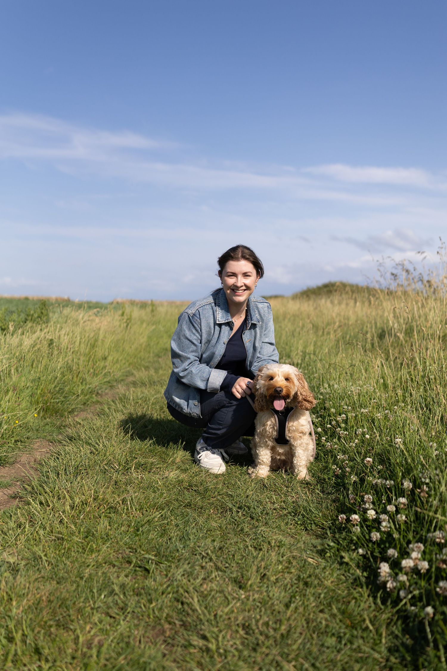 Person and their dog enjoying a sunny day on a grassy hilltop.