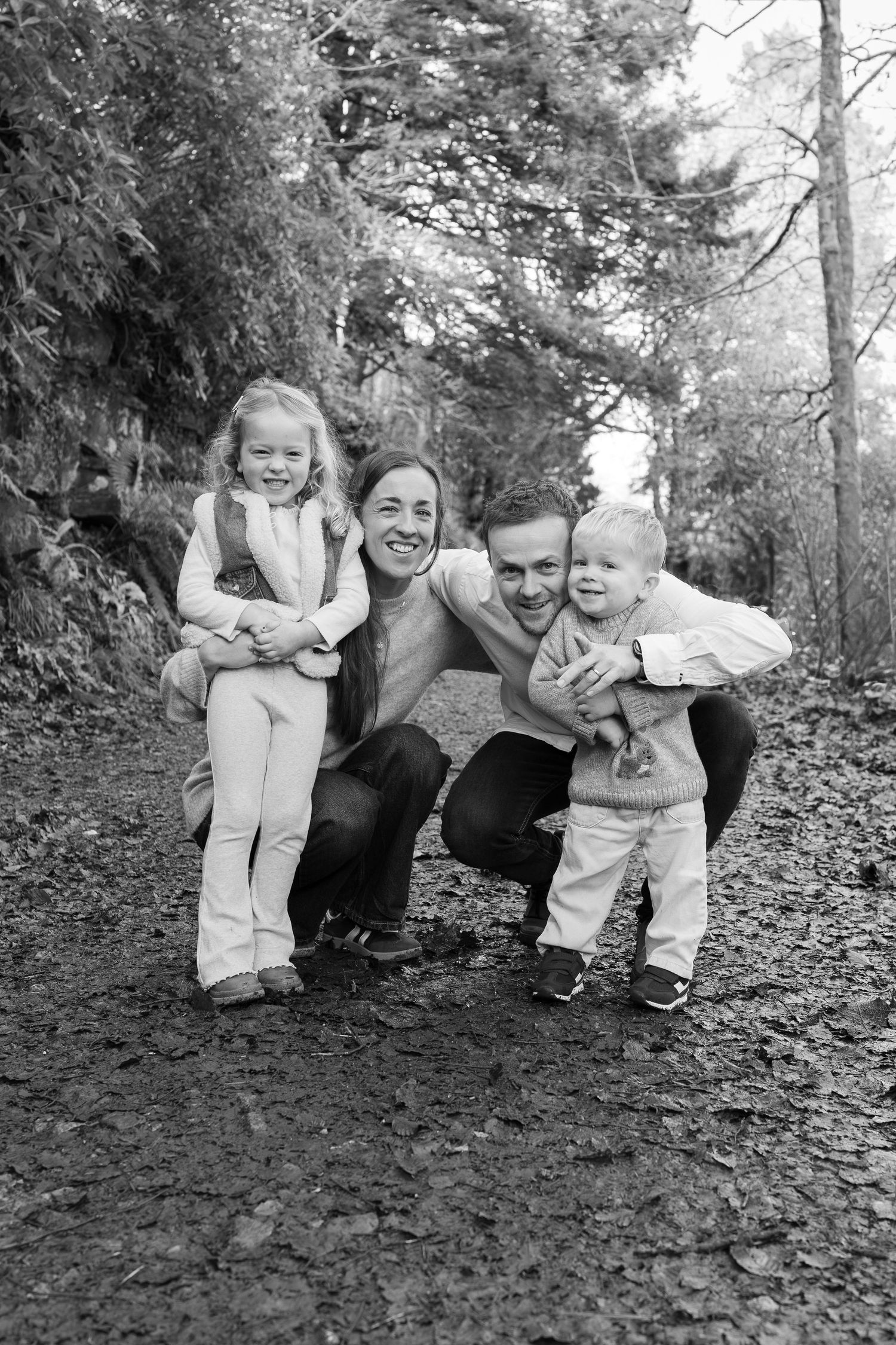 A playful family photo session takes place on a forest hillside.