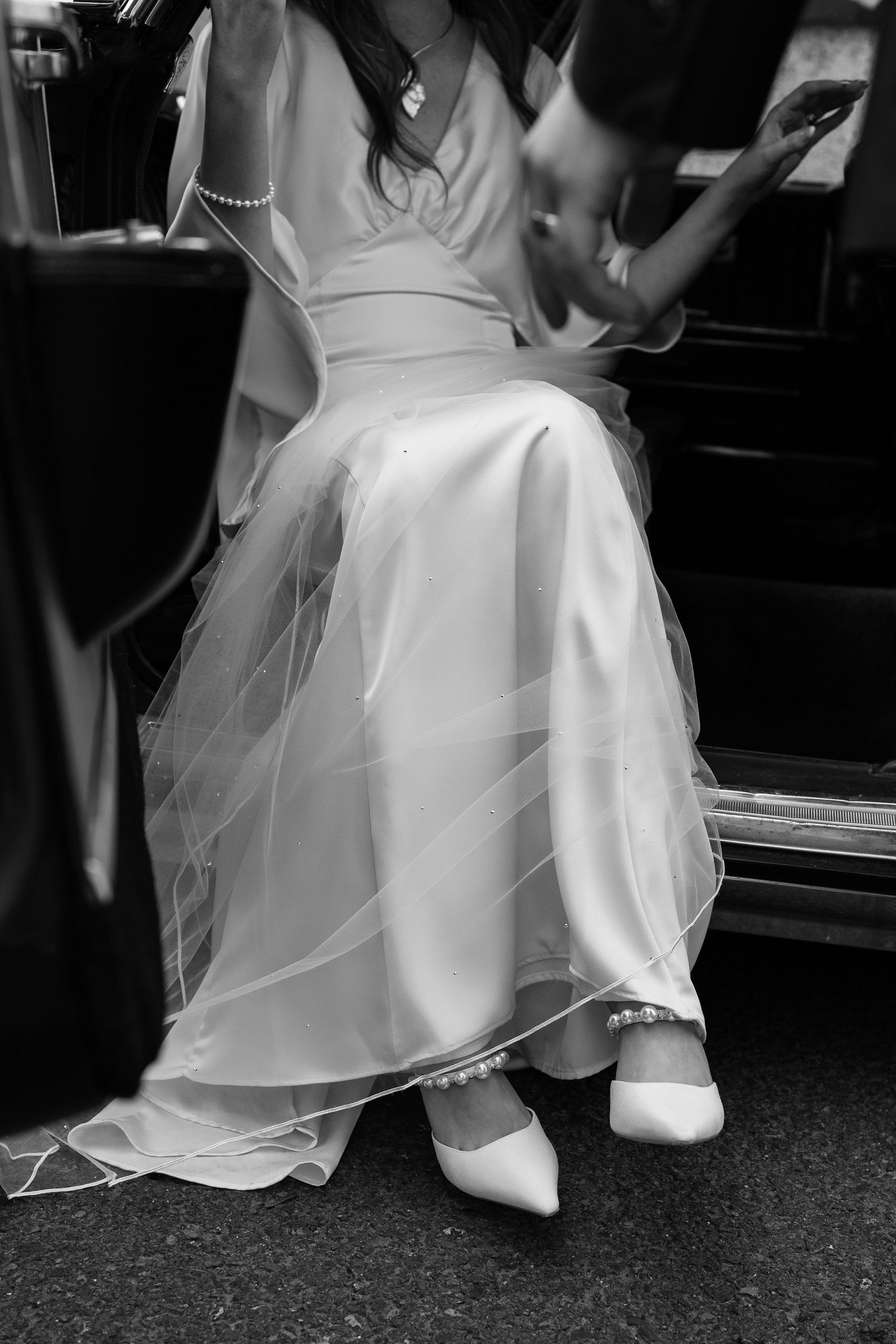 Close-up of a bride's white dress and shoes as she steps into a car.