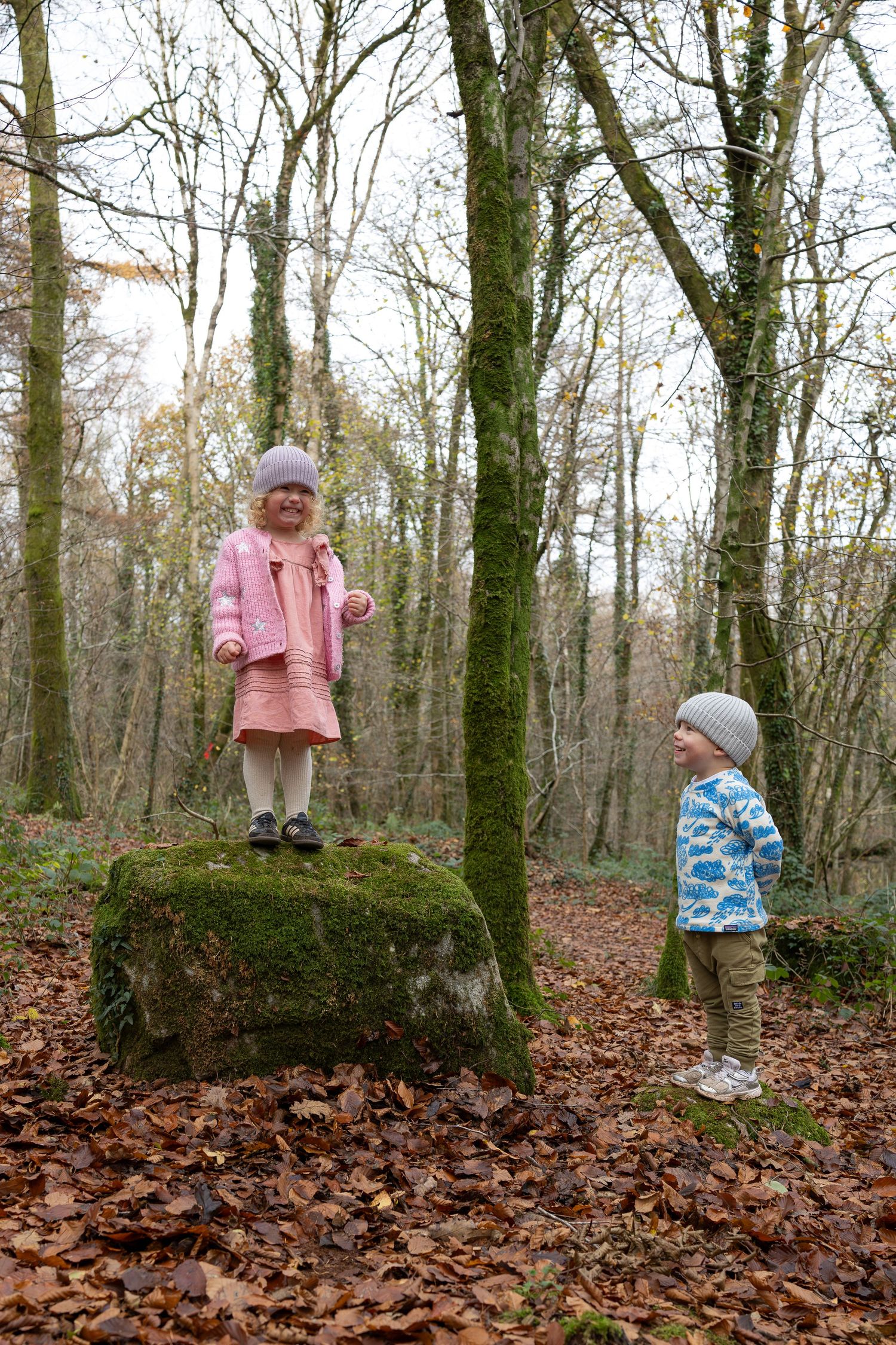 Children play and explore on fallen logs in an autumn forest covered with leaves.