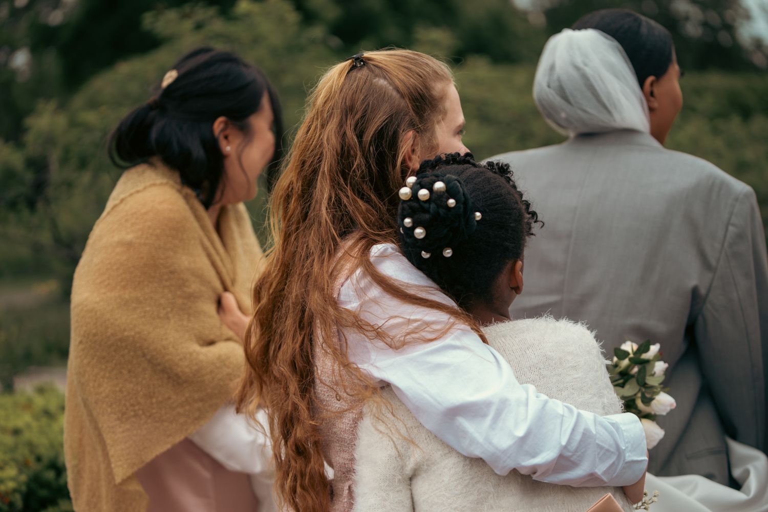Side profile of the couple sister's sharing a soft hug in church lighting, framed with floral pew ends.