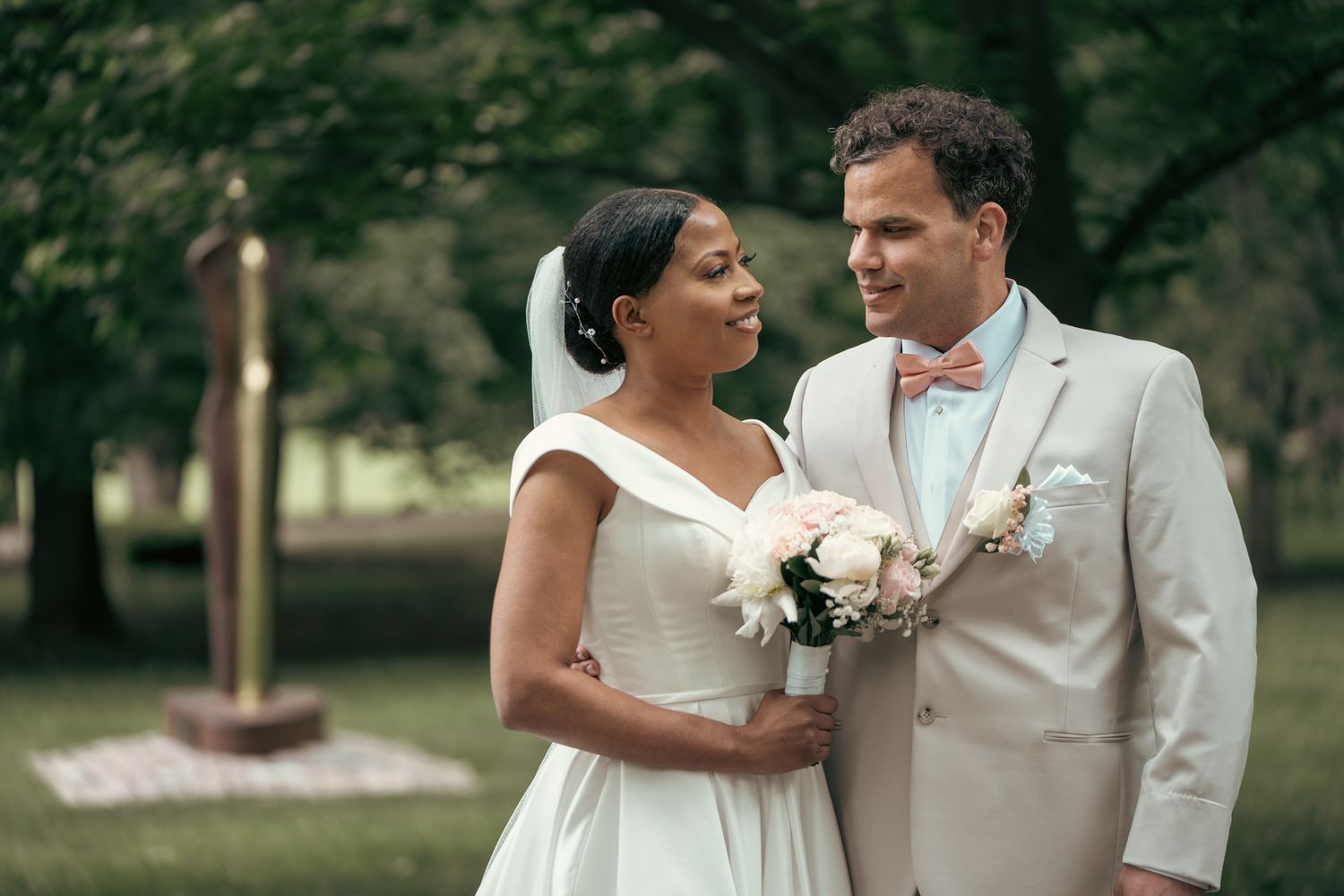 Bride adjusting her veil while the groom watches lovingly during their outdoor portrait session.