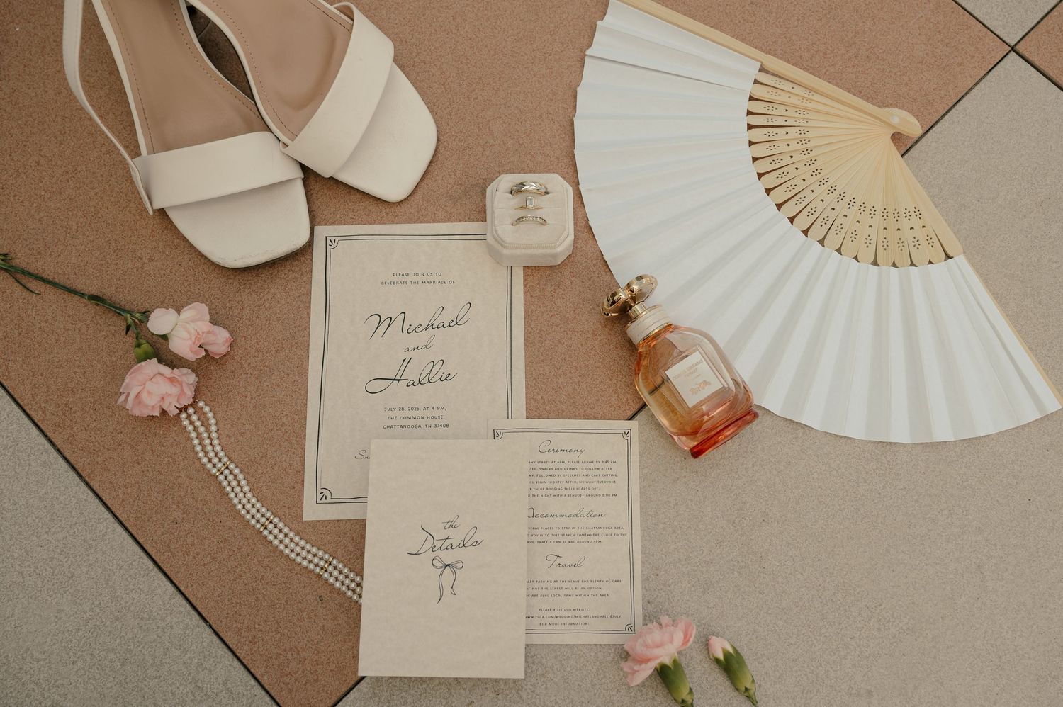 Wedding flat lay featuring invitation suite, white heels, perfume, and a decorative fan.