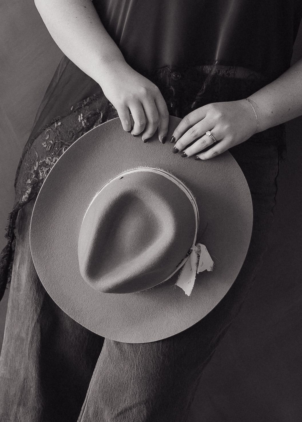 Close-up of hands holding a wide-brim felt hat with ribbon detail in black and white.