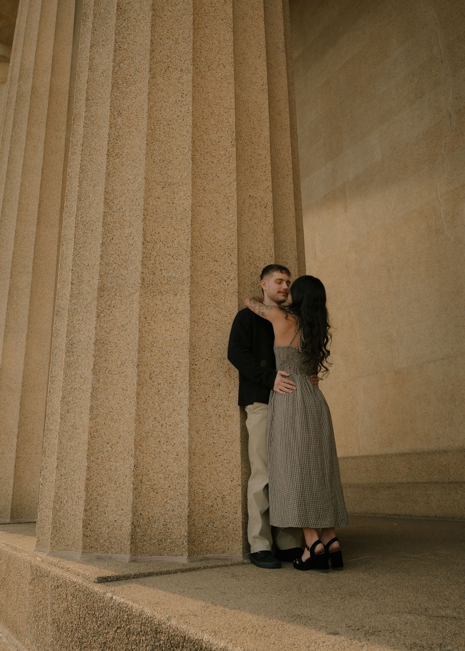 Couple sharing romantic moment between large stone columns at golden hour.