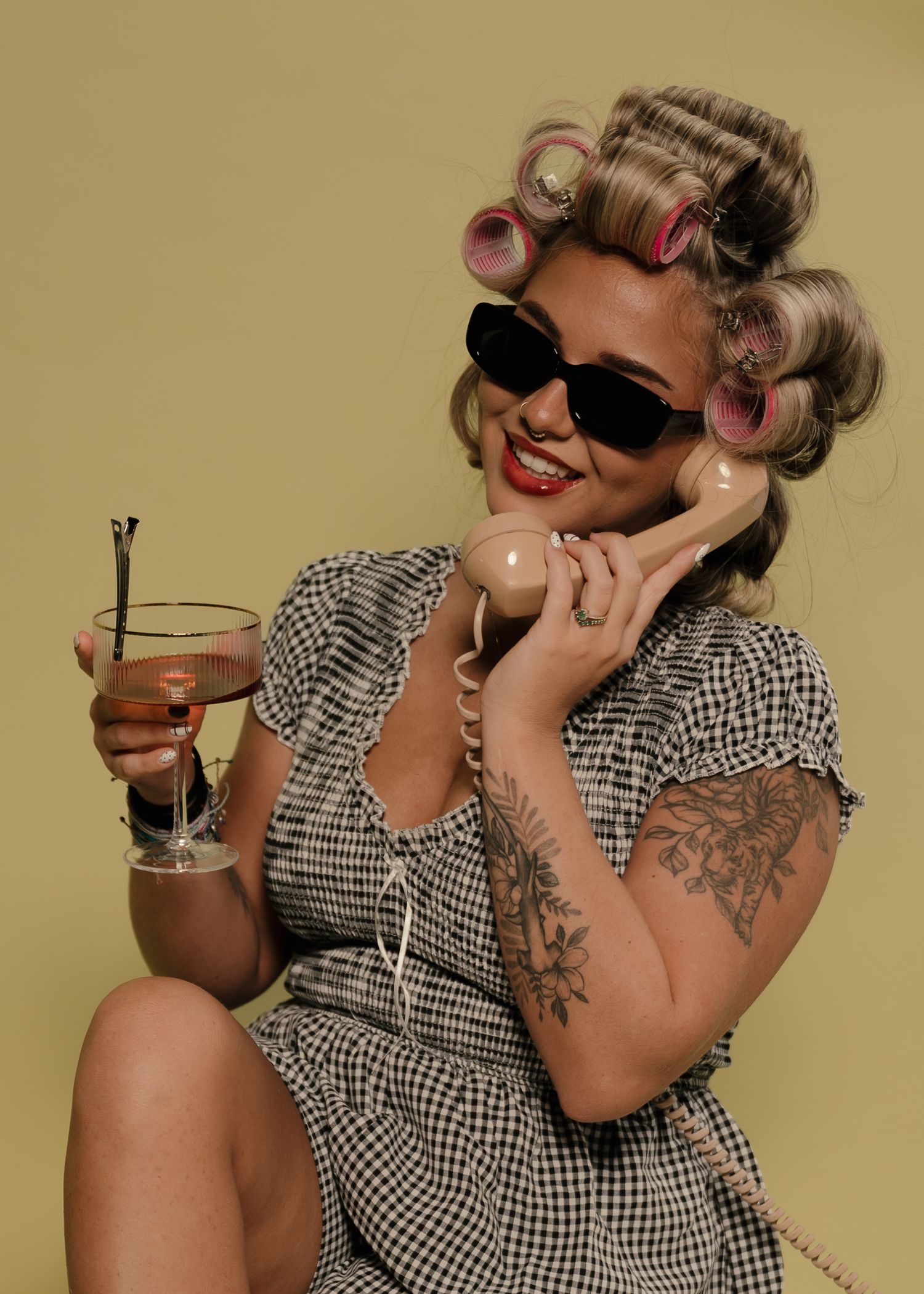Retro pin-up woman with hair rollers, sunglasses, holding cocktail and vintage telephone.