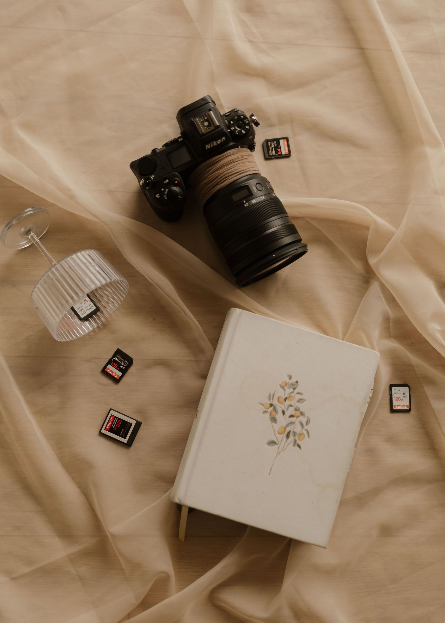 Flat lay of Nikon camera, journal, memory cards, and accessories arranged on beige fabric.