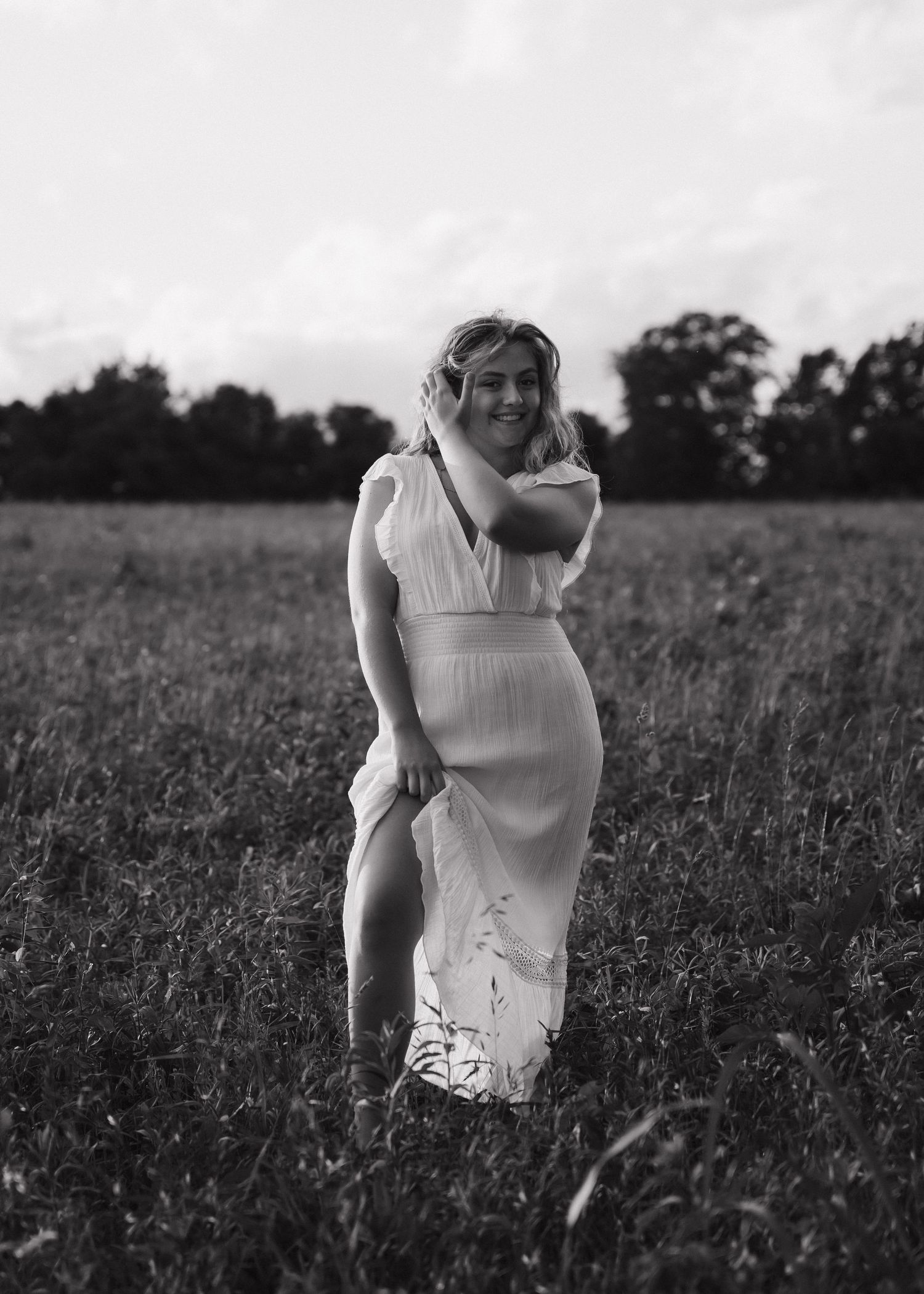 Black and white photo of a blonde woman in a white dress walking through a grassy meadow.