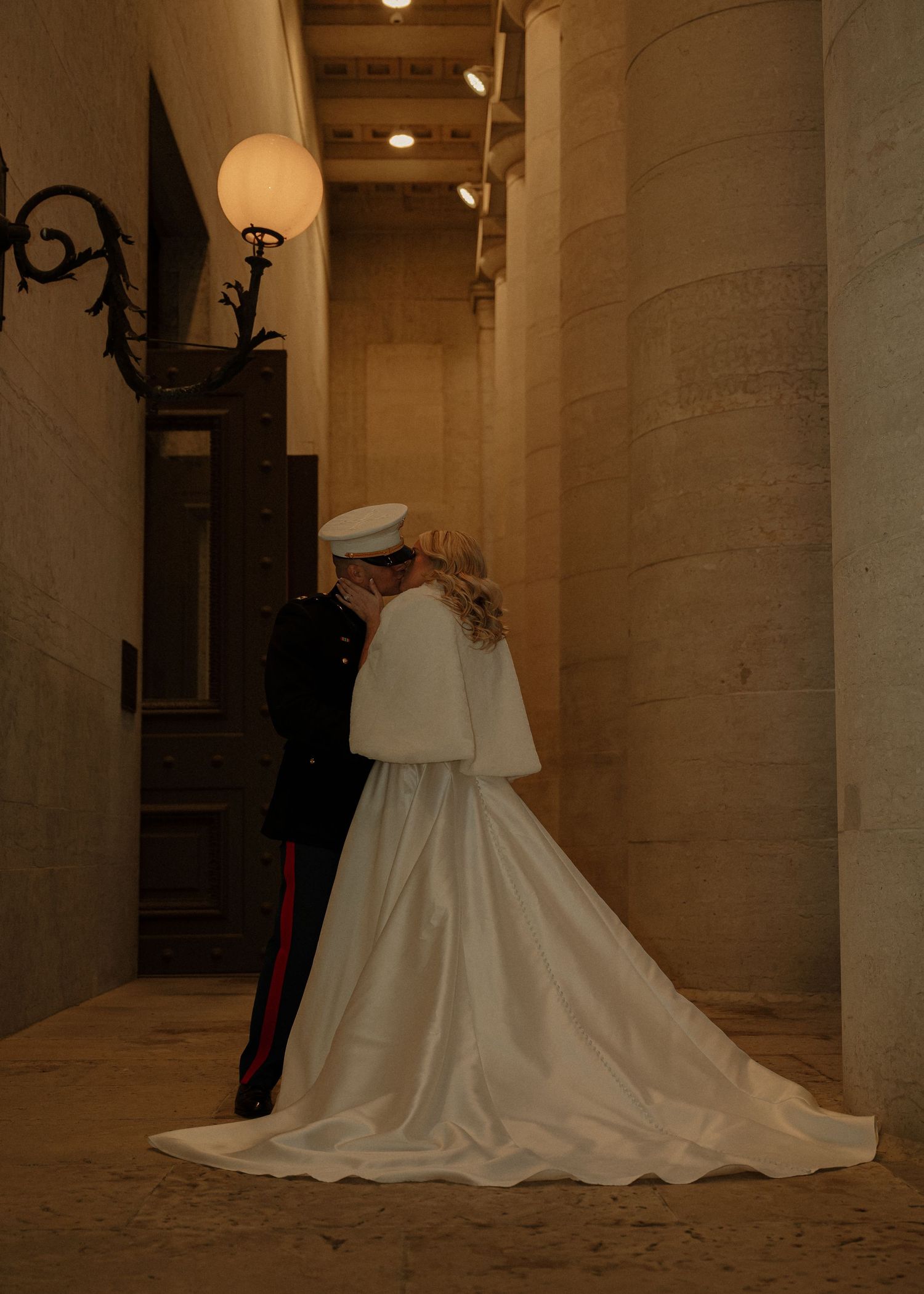 Bride in white cape gown and Marine groom share an intimate moment in ornate stone corridor at wedding. Columbus, Ohio State House Portraits